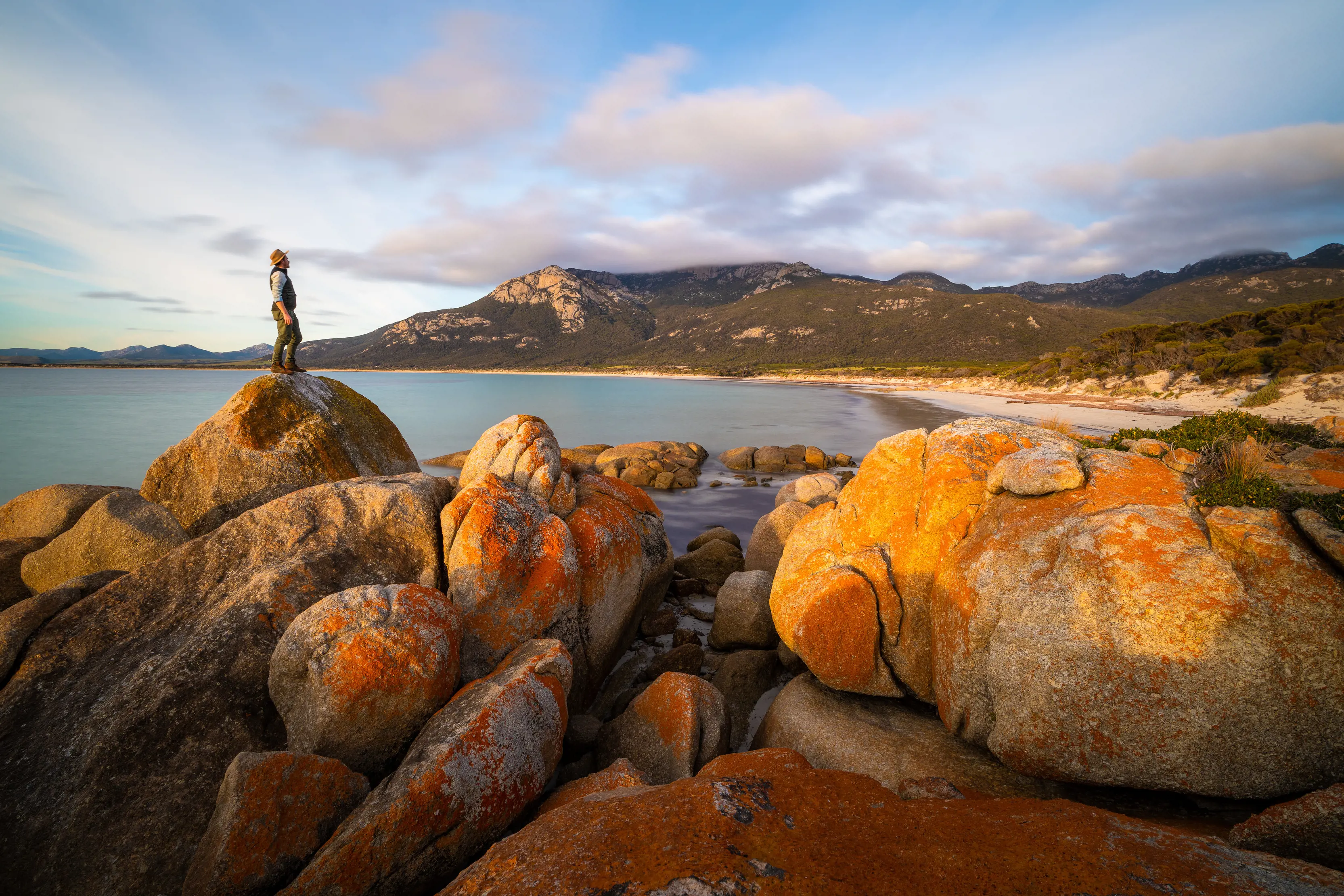 Breathtaking image of Fotheringate Bay, Flinders Island, of a man standing on a large rock, looking over the stunning coastline.