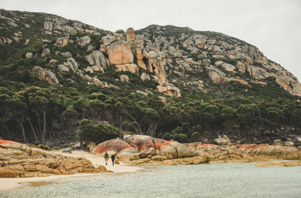 Two people walking along the sand,by the ocean at The Dock and lower slopes of Mt Killiecrankie, Flinders Island.