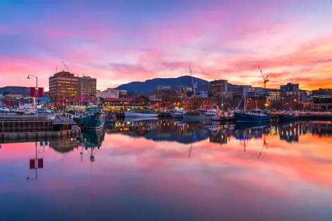 Hobart waterfront at sunset. Hues of pink, purple and orange hitting the skyline and water