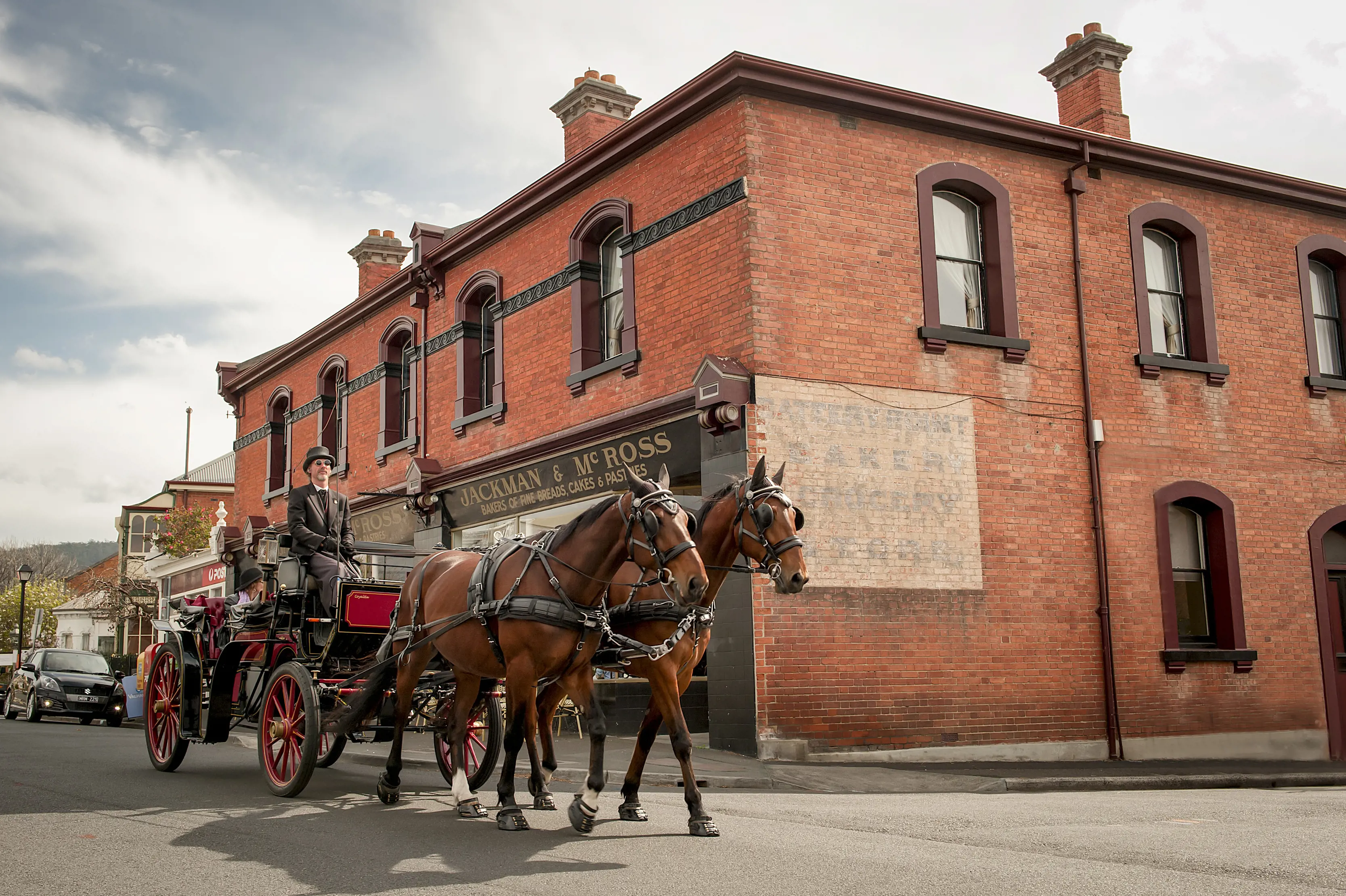 A horse drawn carriage, pulled by two large horses moves down a Hobart street, with a red brick building in the background.