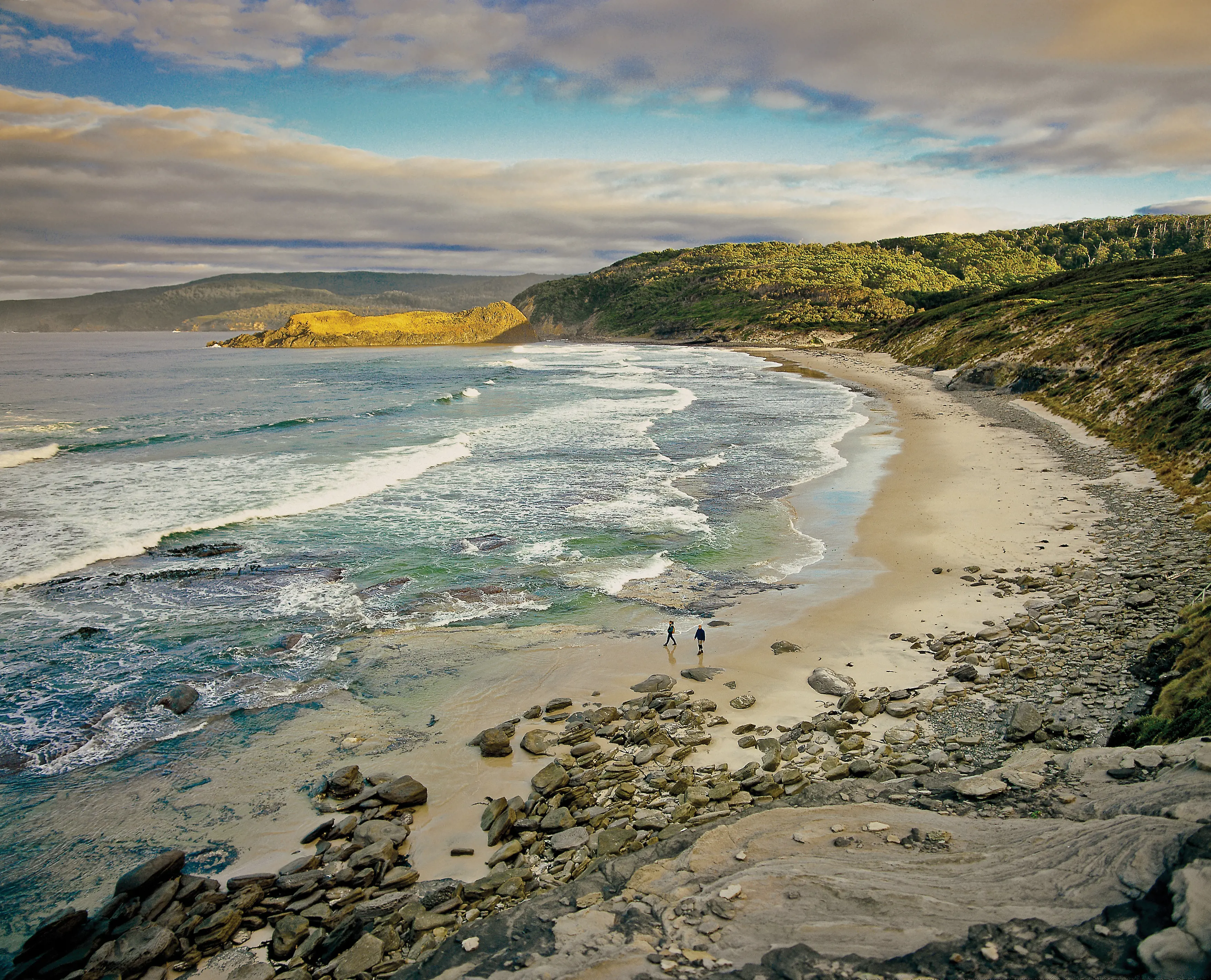 Wide landscape with two people walking along South Cape Bay, Cockle Creek. The look small amongst the vast landscape.