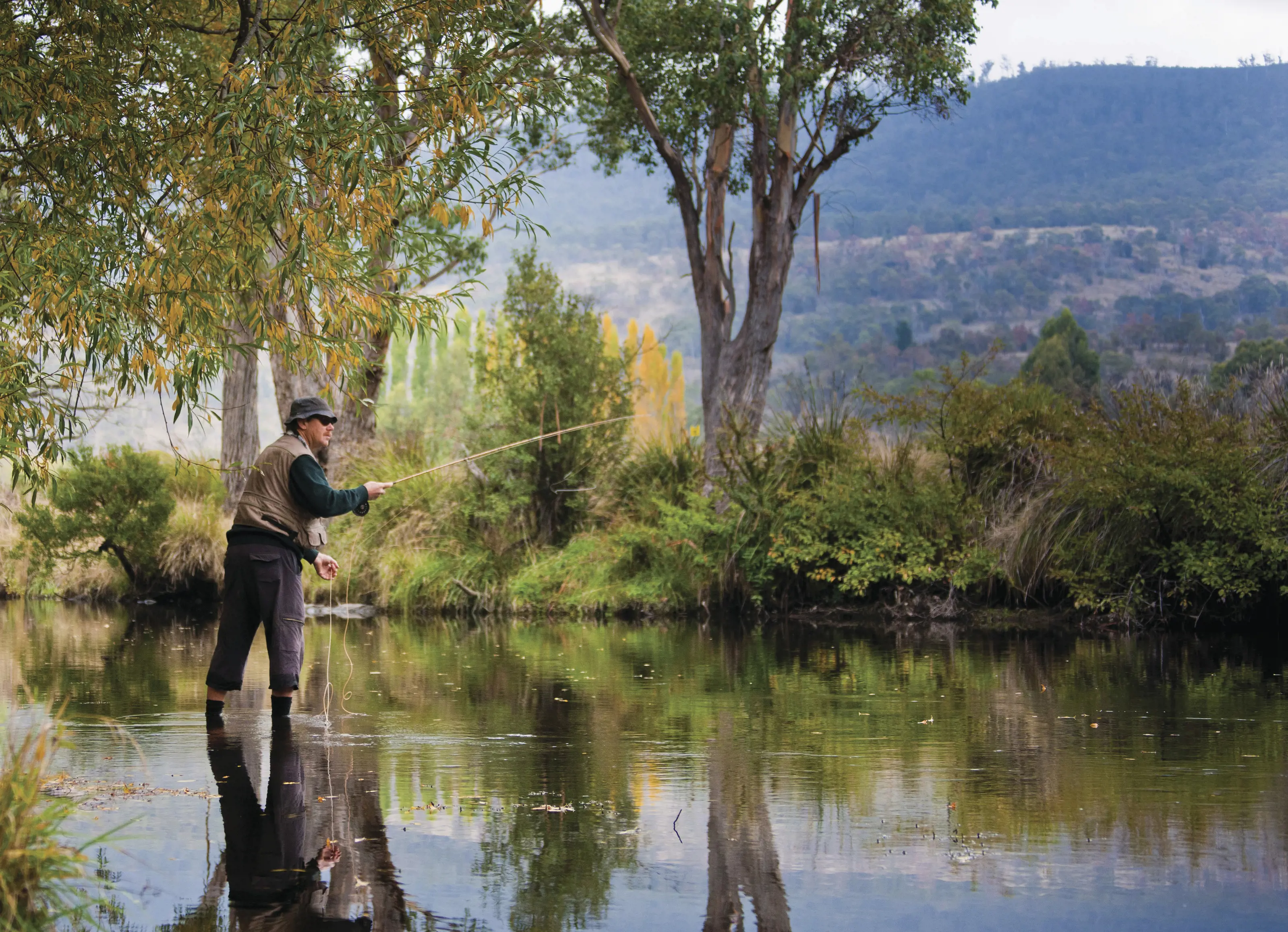 A fly fisher casts his rod whilst standing in shallow waters at the Tyenna River.