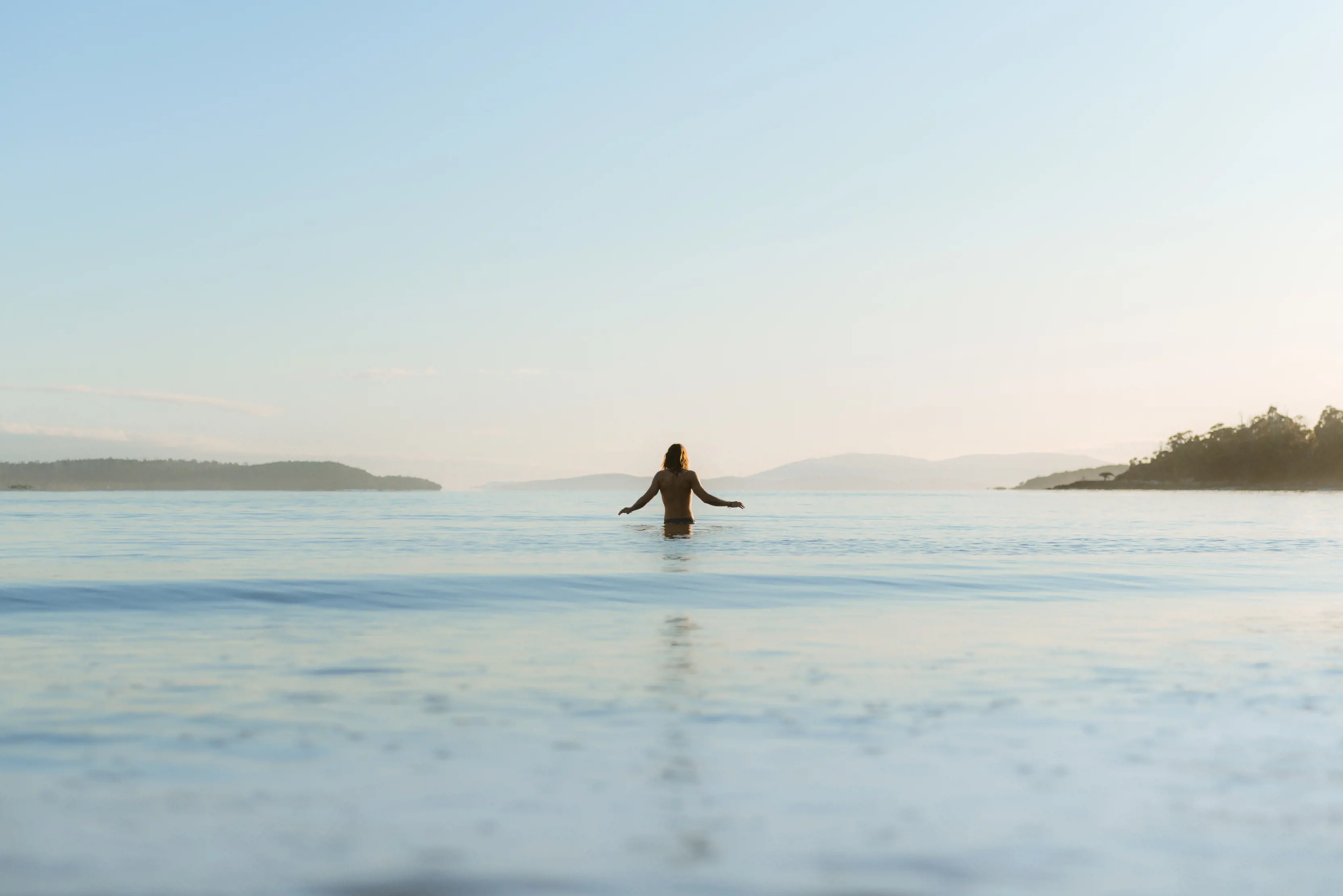 A man walks into the water at Cockle Creek, the camera is behind him.