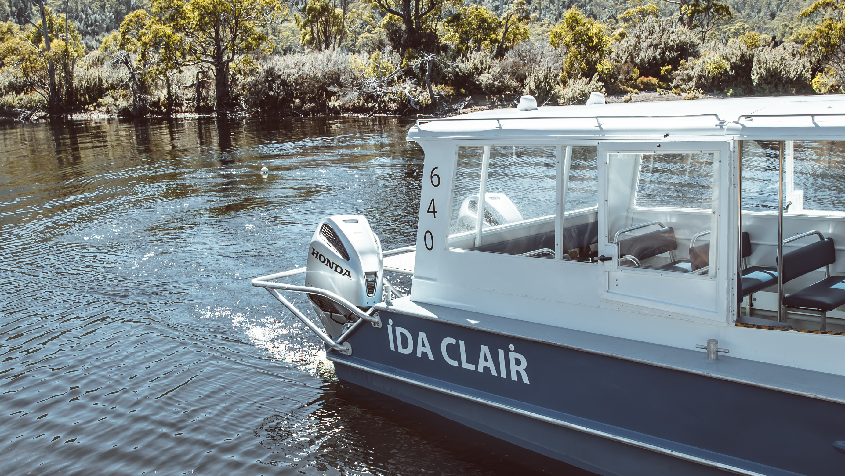A navy and white boat, with IDA CLAIR, written on the side crosses the water at Lake St Clair National Park.