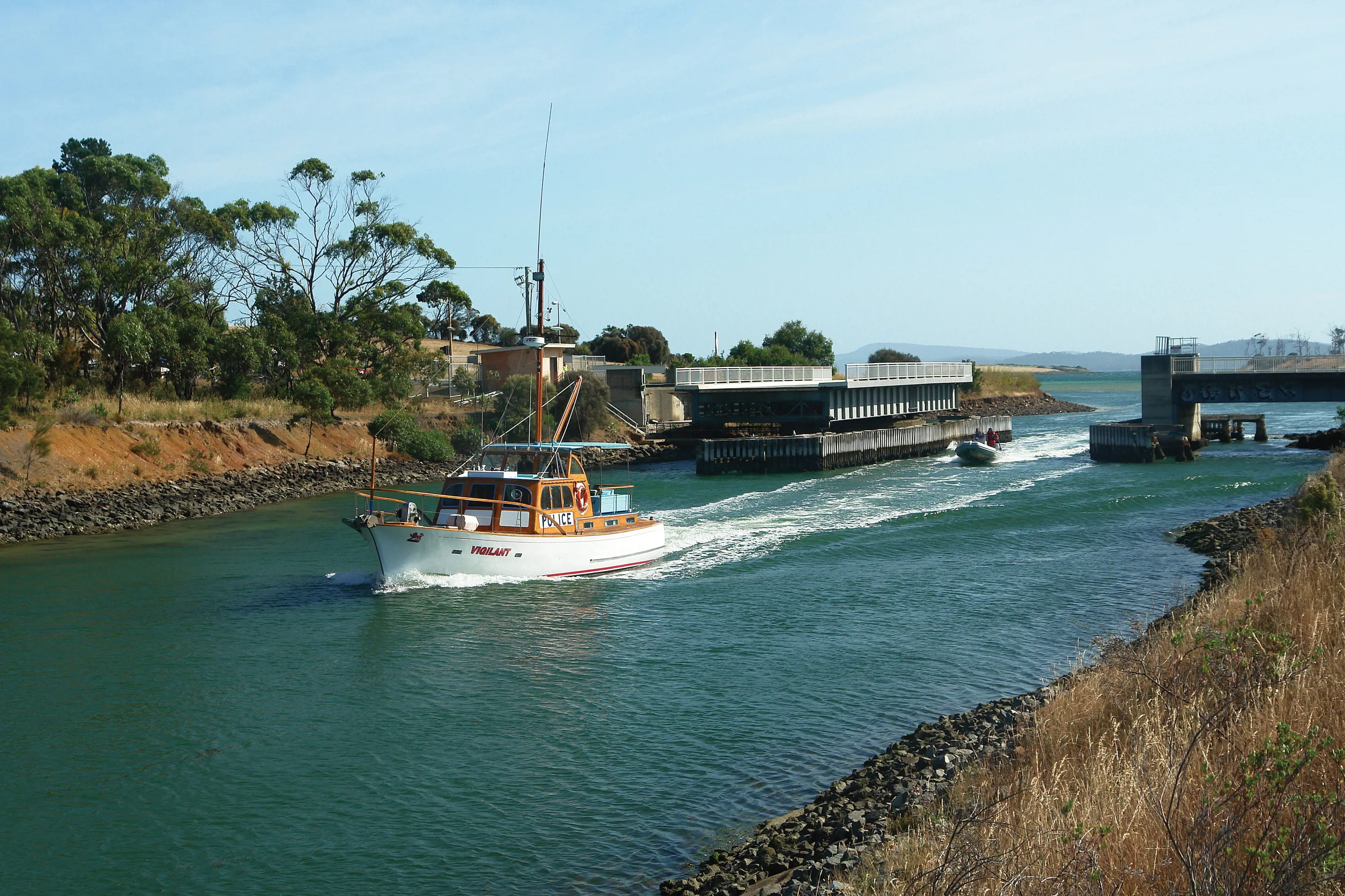 A white and wooden boat passes through the Denison Canal.