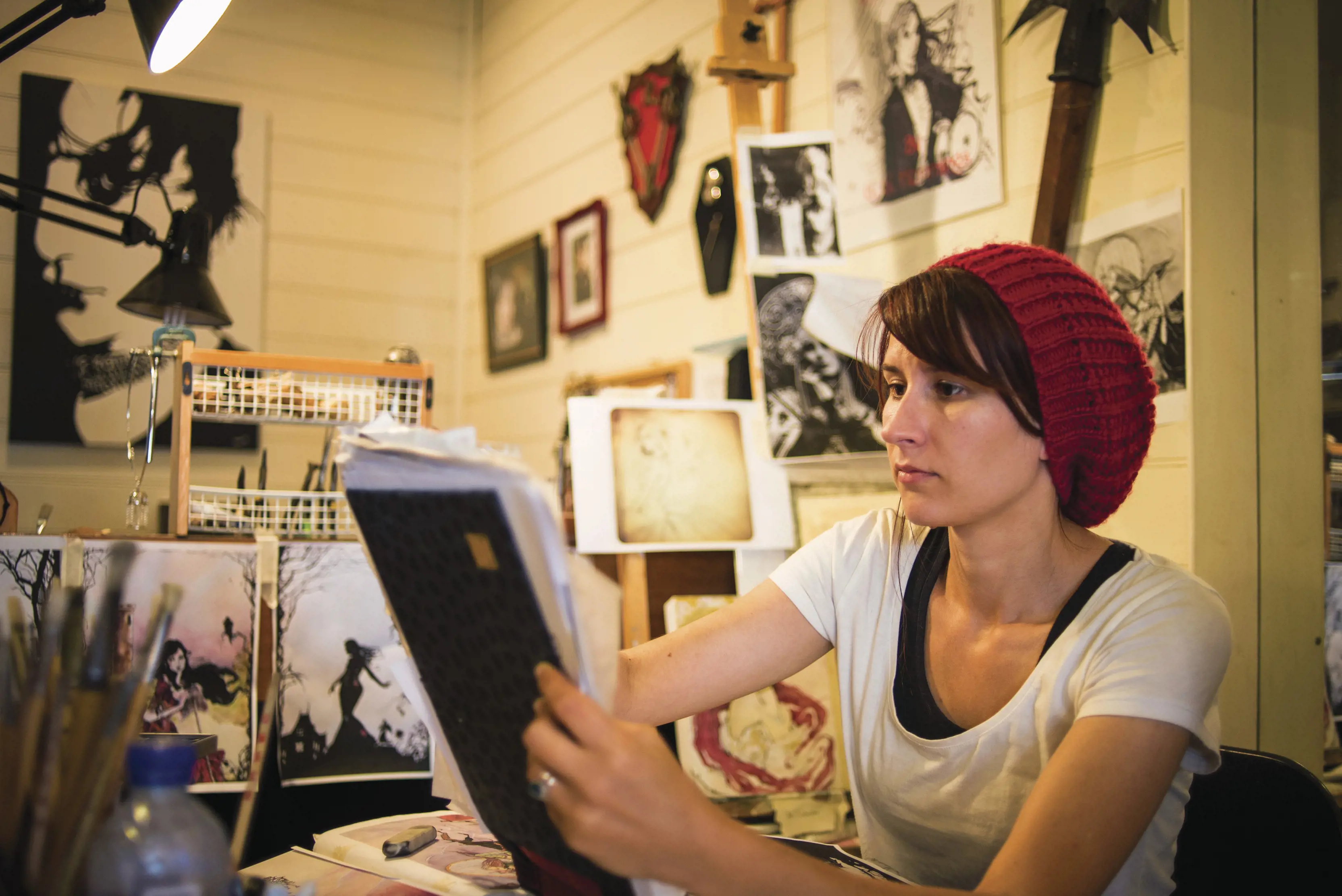 Close up of a designer at work in the foreground, the wall is covered with art work in the background at Cobweb Designs.