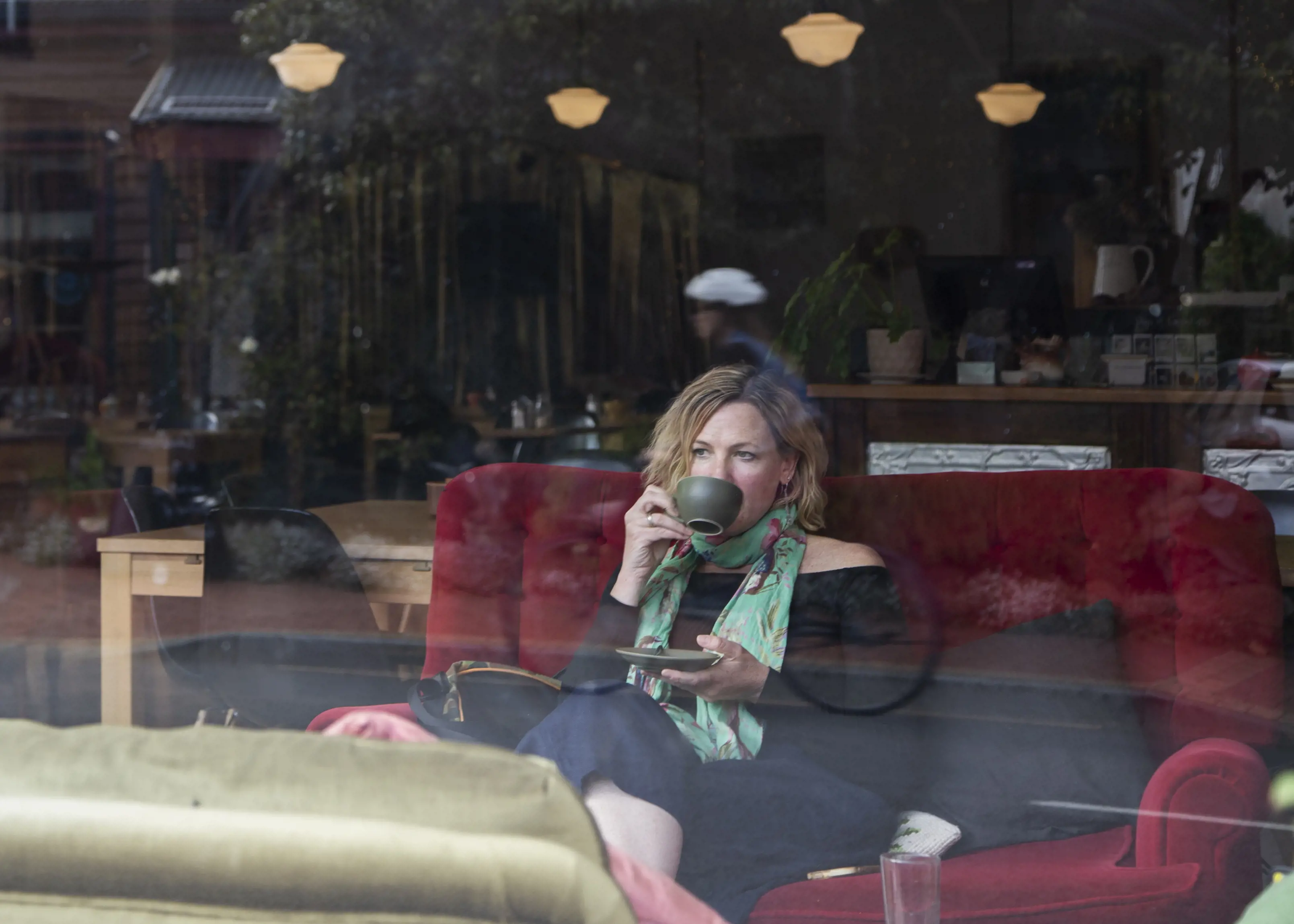 A woman sips on coffee whilst sat on a red sofa at The Red Velvet Lounge.