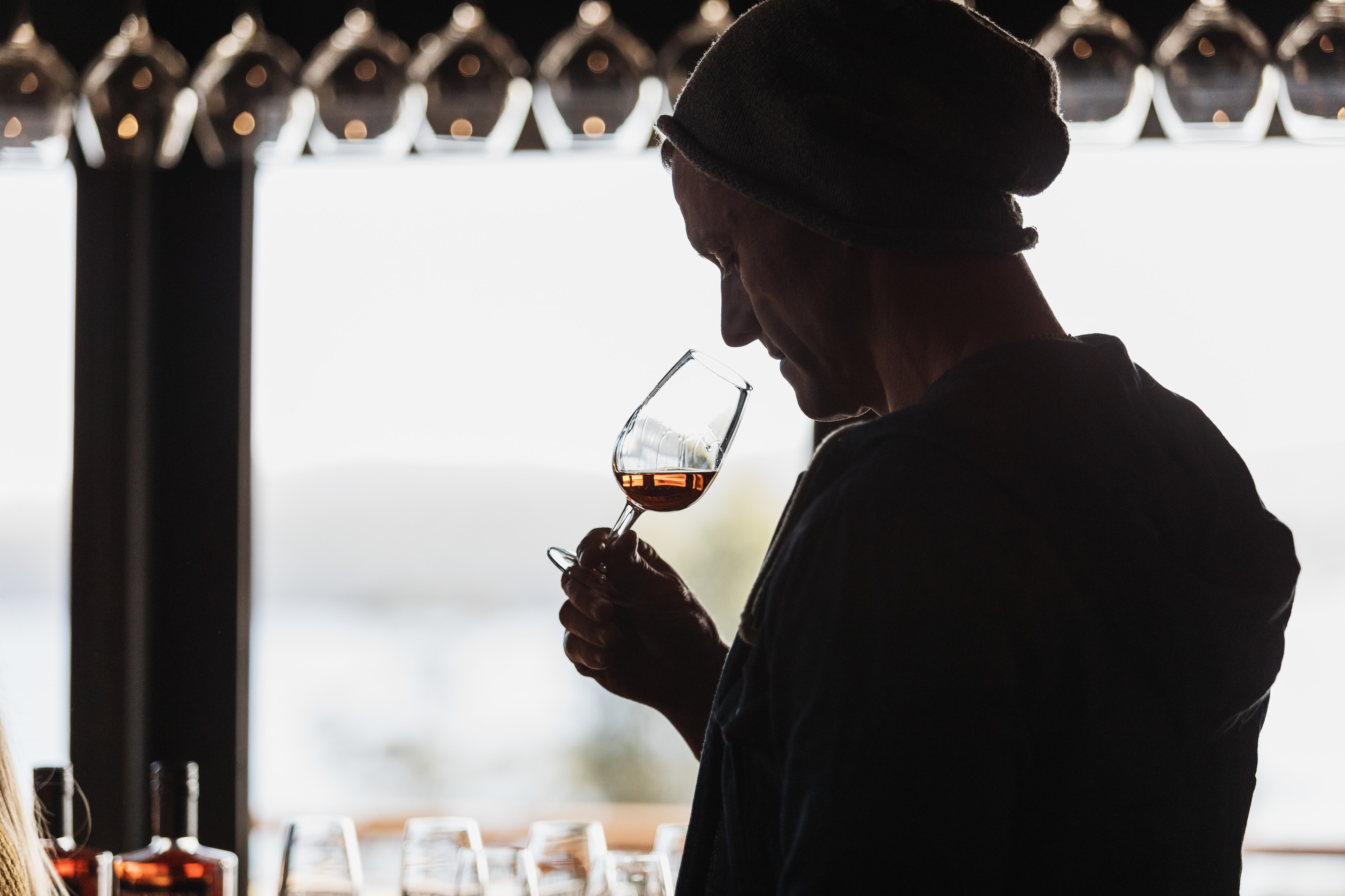 Close up, moody image of a person wearing a beanie, smelling a glass of whisky.