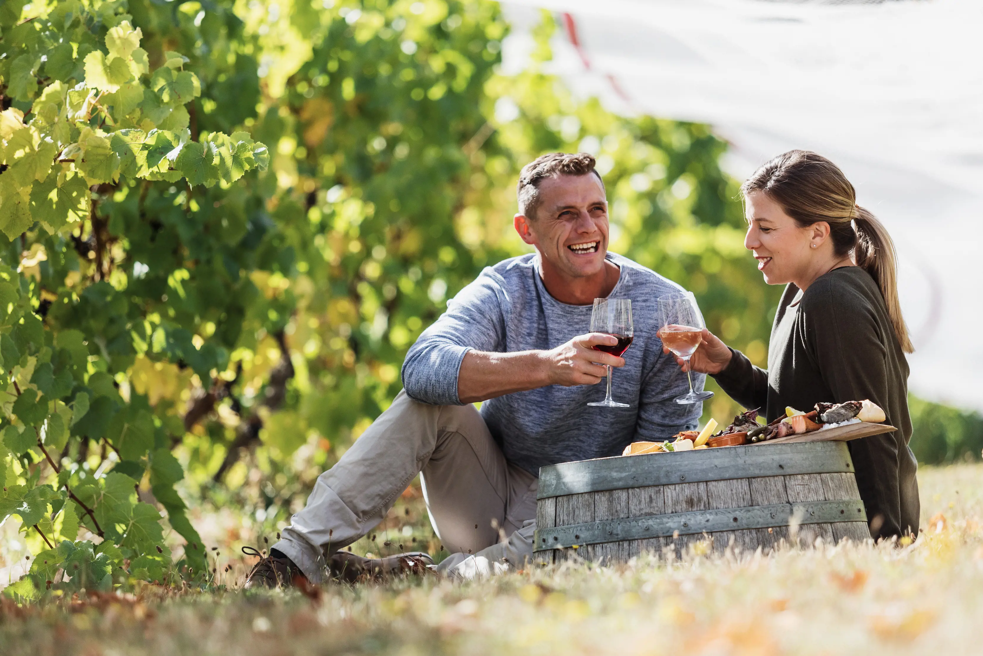 A couple laughing and enjoying a glass of wine and a food platter by the vineyards at Bruny Island Premium Wines.