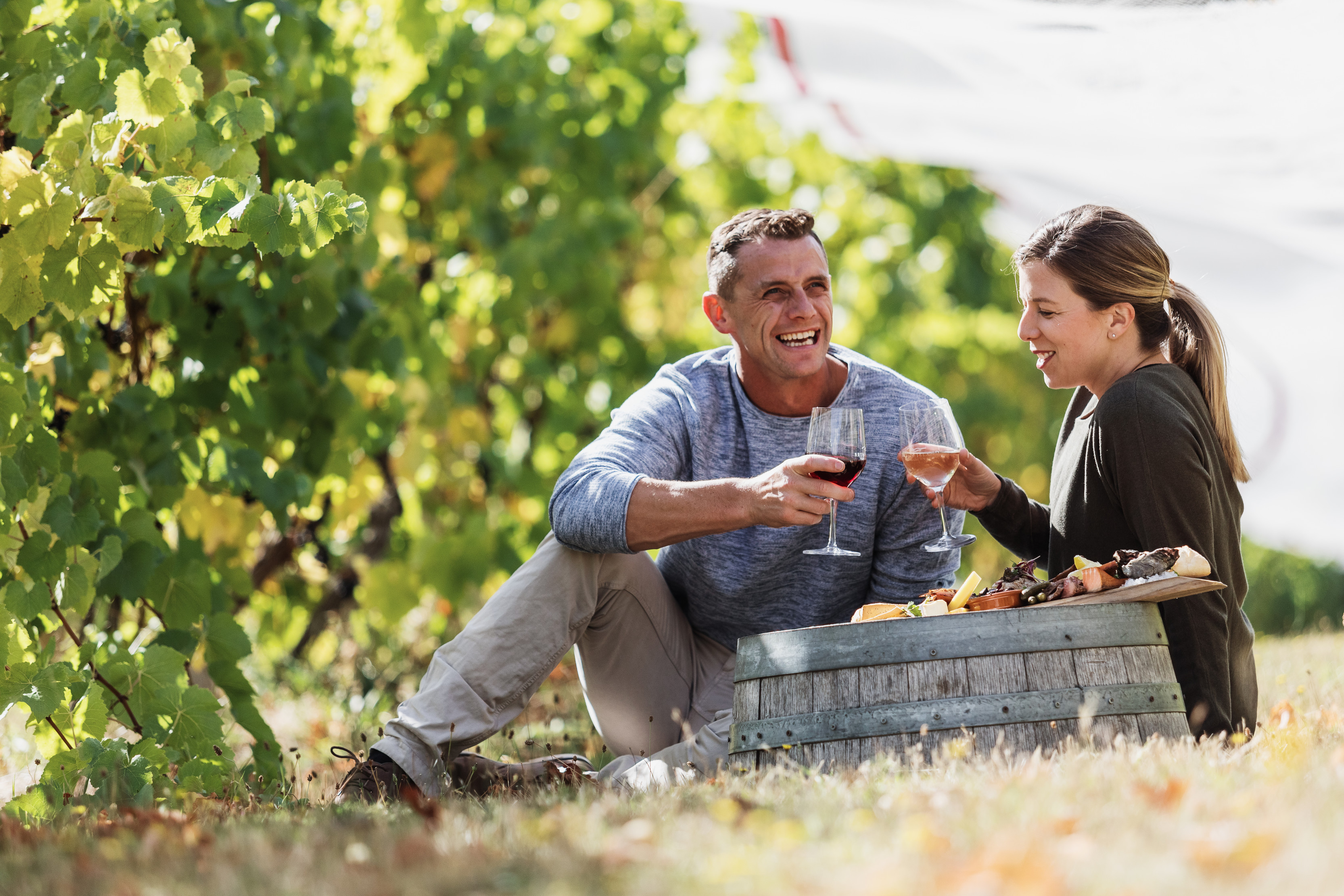 A couple laughing and enjoying a glass of wine and a food platter by the vineyards at Bruny Island Premium Wines.