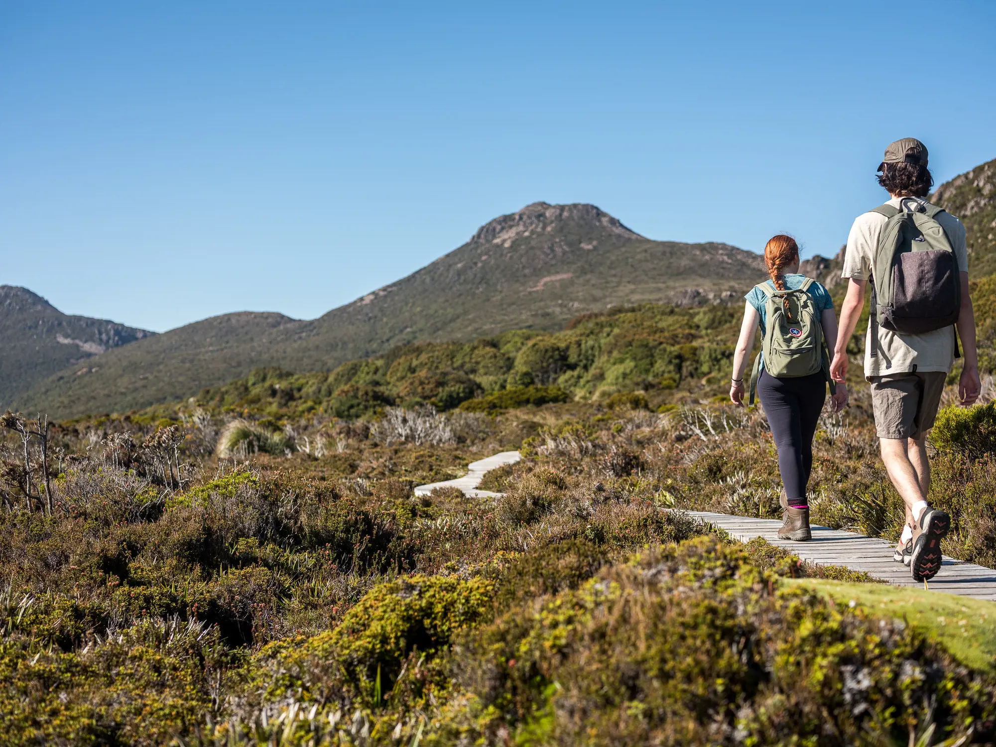 A couple walk along the footpath at Hartz Mountains National Park, with mountains in the back drop.