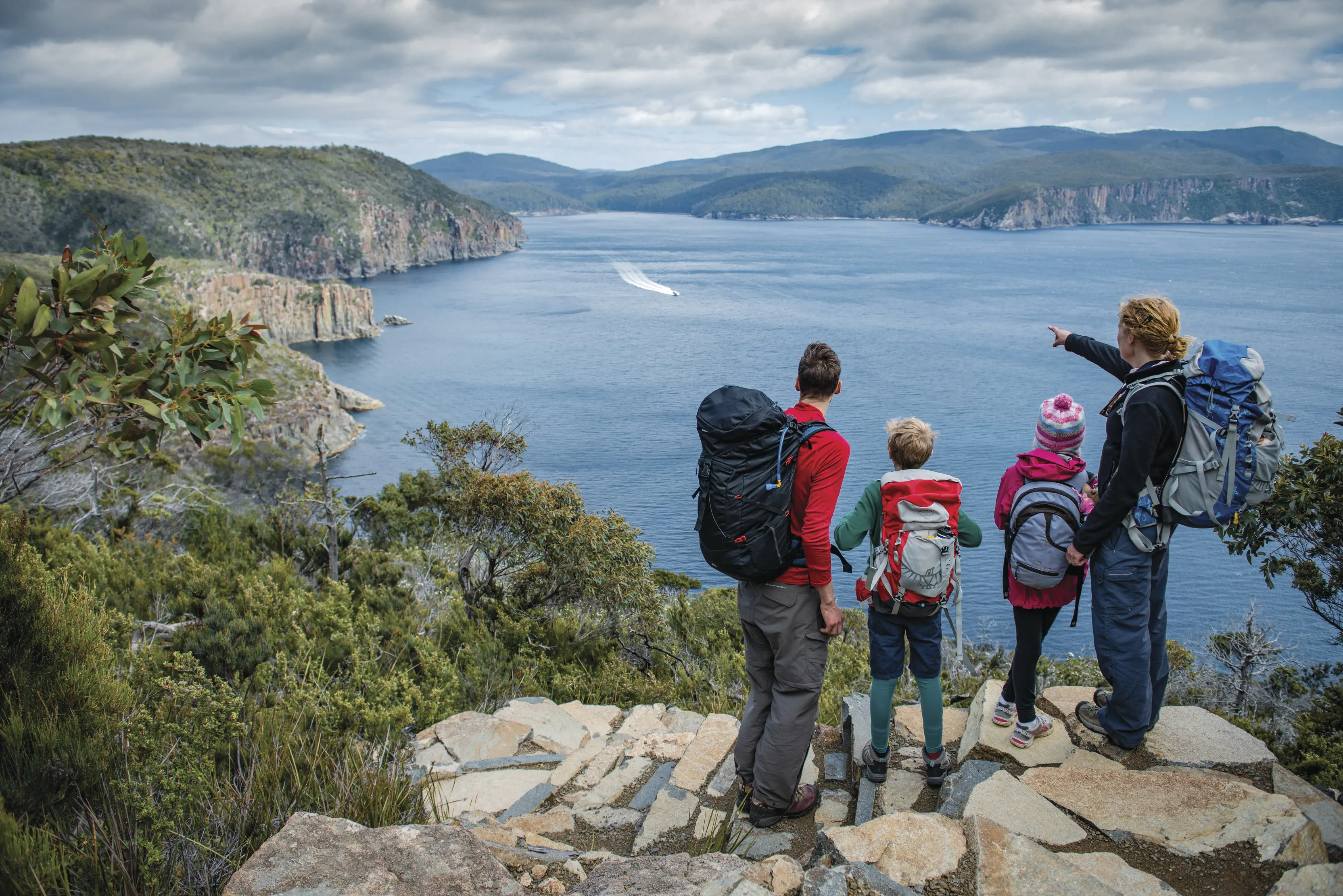 A family stop and look over the cliff at Cape Hauy, Three Capes Track, pointing at the view.