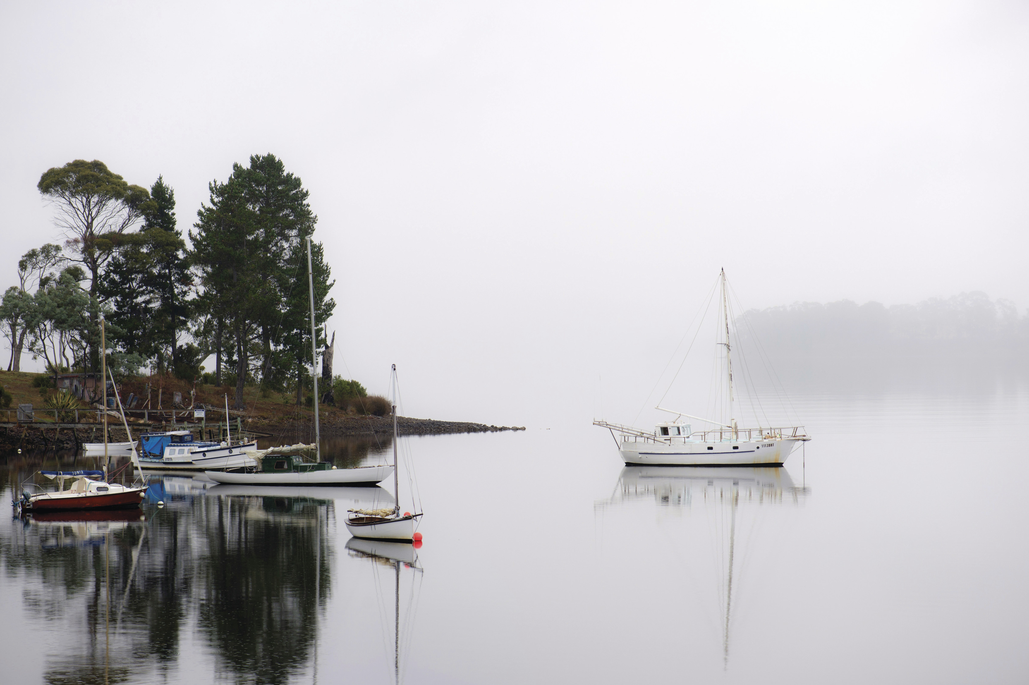 Boats on the misty Huon River. The sky blends into the water as it's covered by the mist.