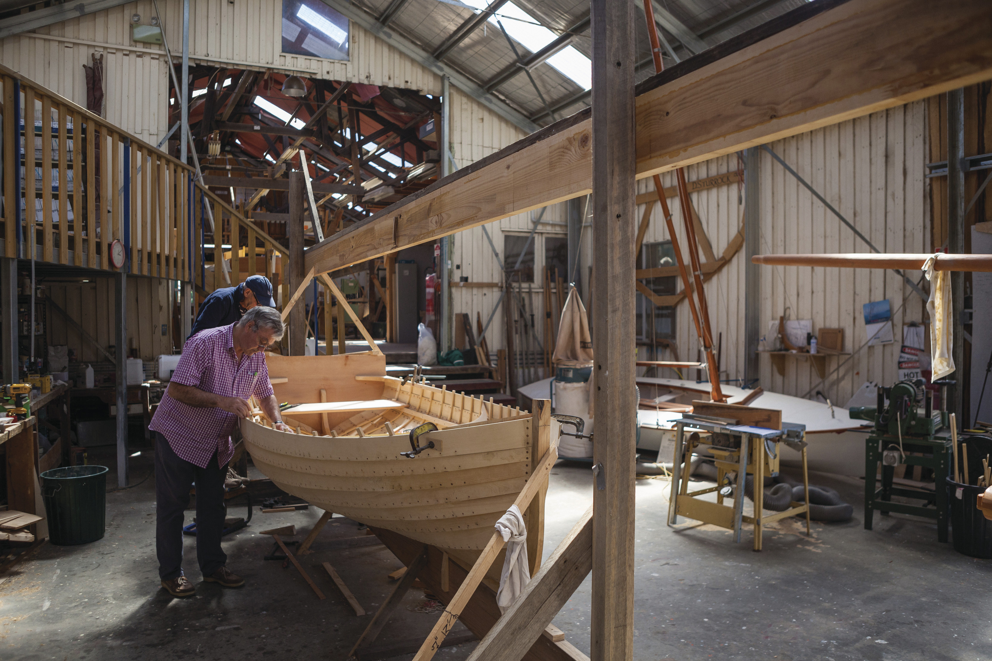 Two men looking into small wooden boat in a boat shed at the Wooden Boat Centre Tasmania