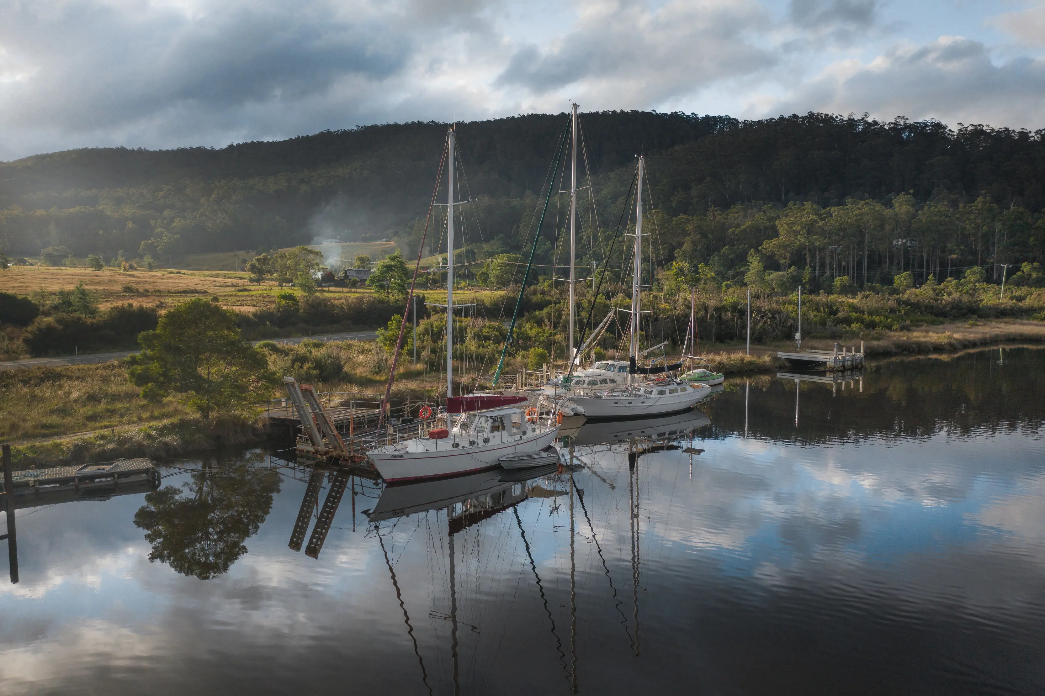 Two fishing boats floating on the water in Franklin. The boats are reflecting off the glossy, missor-like lake. Mountains in the background