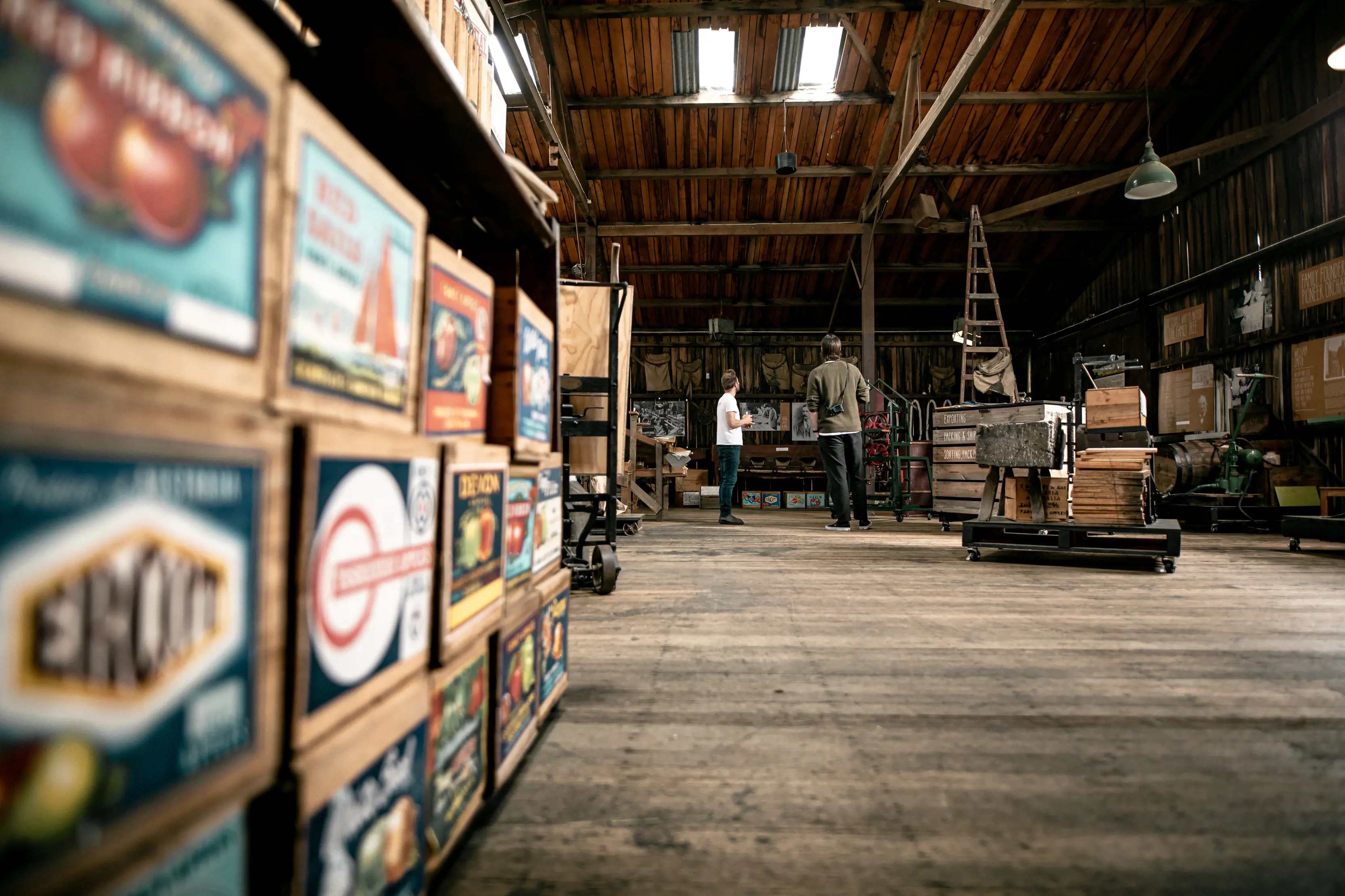 Two people standing around an apple shed. You can see vintage boxes placed on the shelves at Willie Smith's Apple Shed