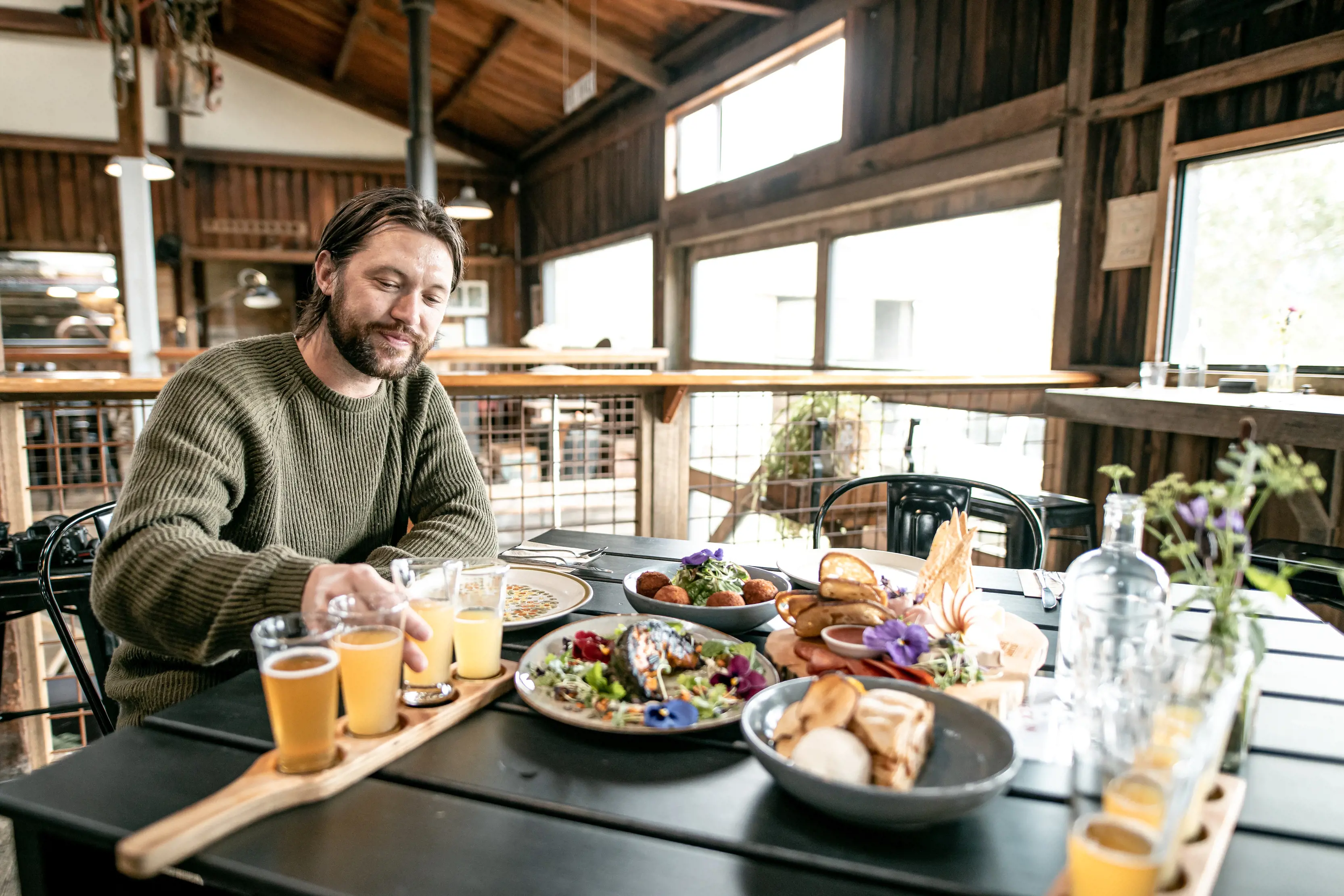 Man enjoying a paddleboard full of various beers and a table filled with delicious foods at Willie Smith's Apple Shed