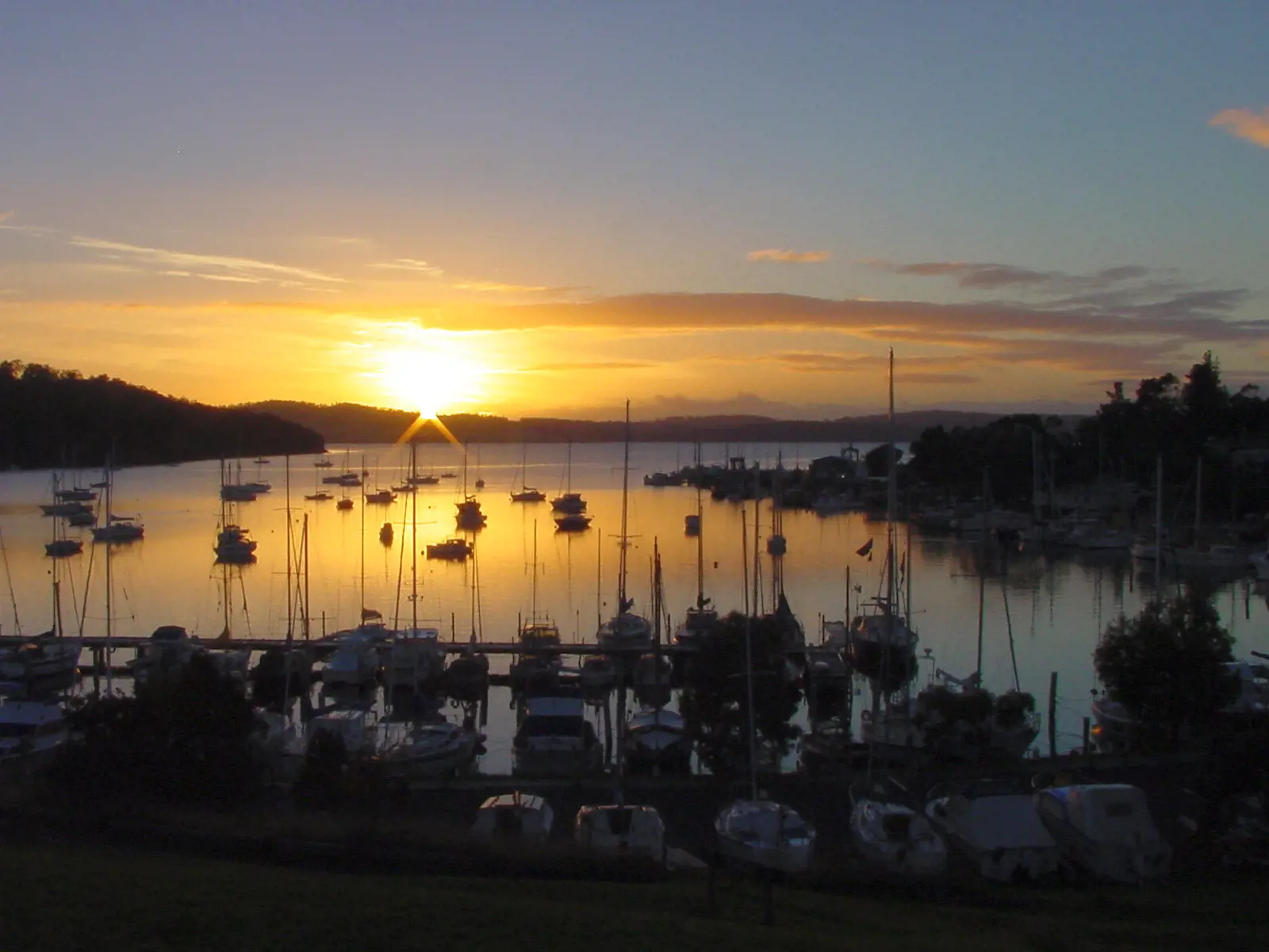 The sun sets over a calm ocean bay filled with moored boats in Kettering.