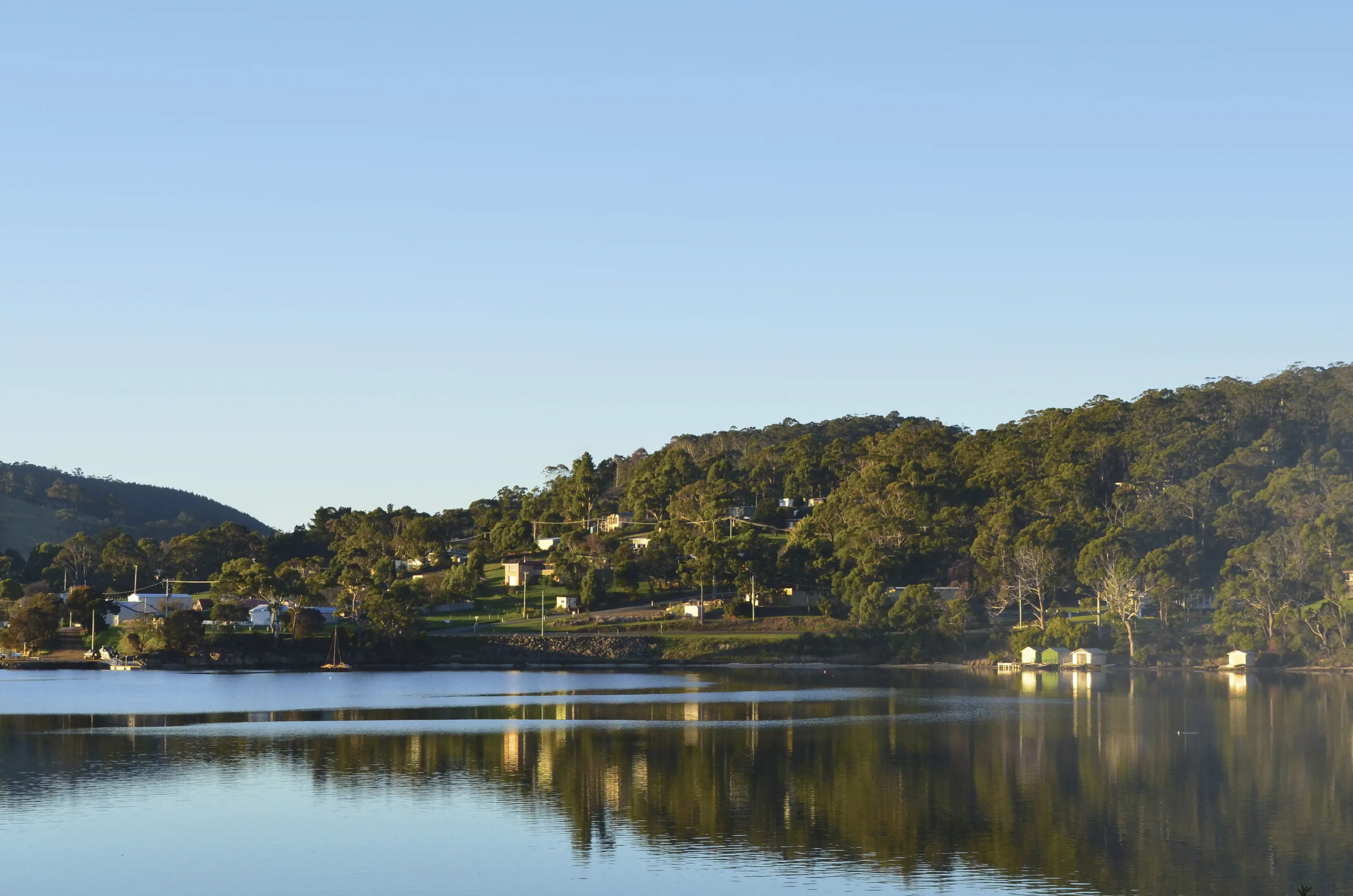 Looking over a calm bay with houses dotted amongst the trees in the distance, at Nubeena waterfront.