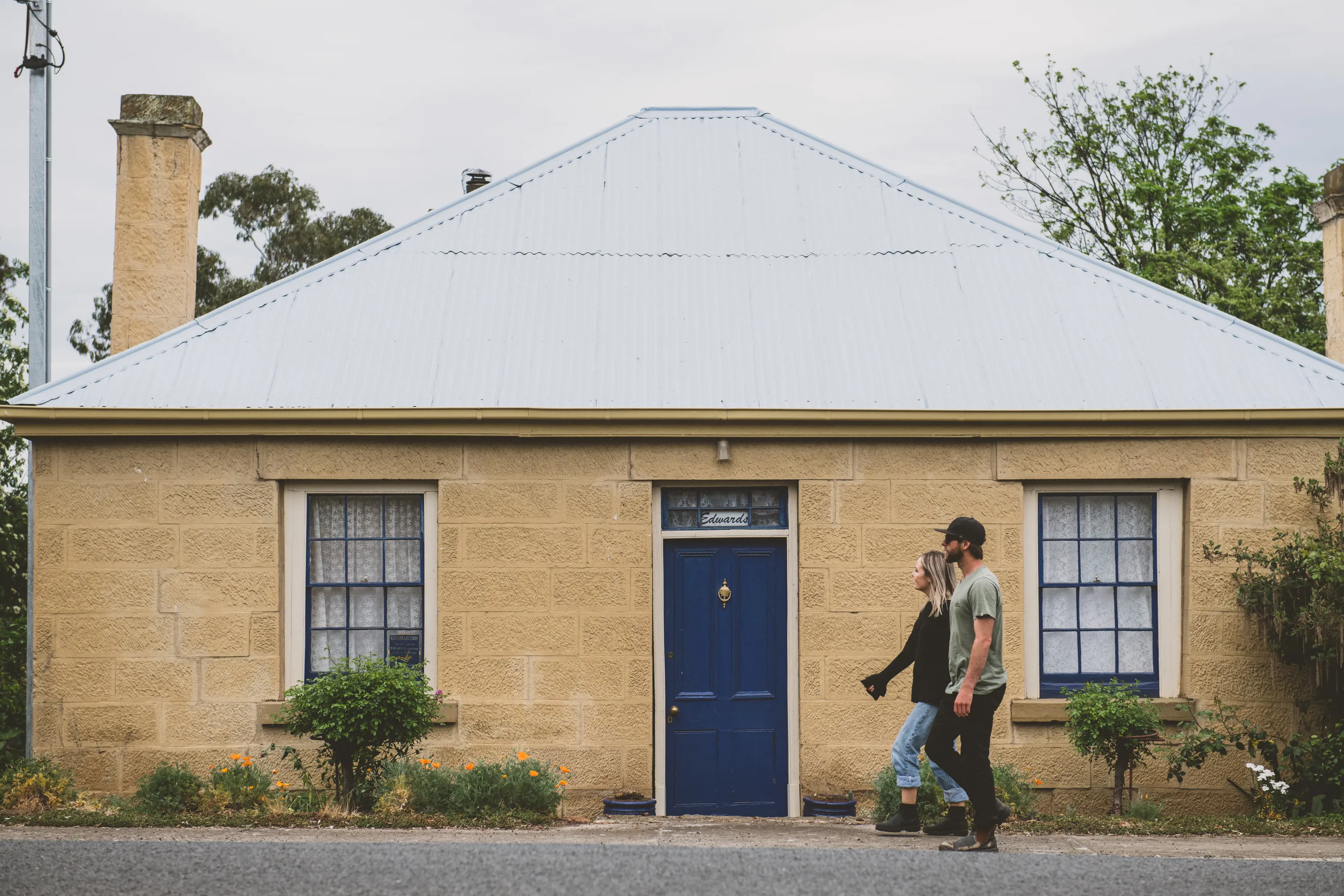 A couple walk past a cottage with a blue door whilst exploring in Hamilton.