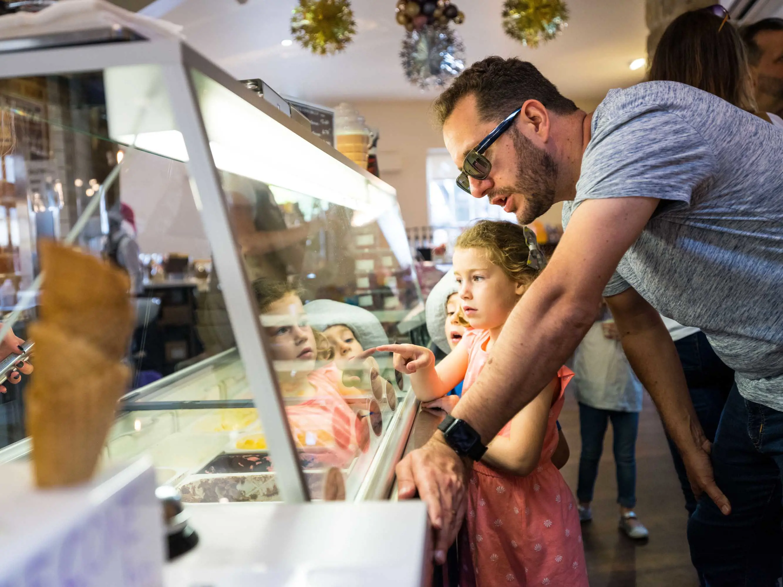 A midle-aged man stands at a ice cream counter with his daughter choosing from the flavours available.