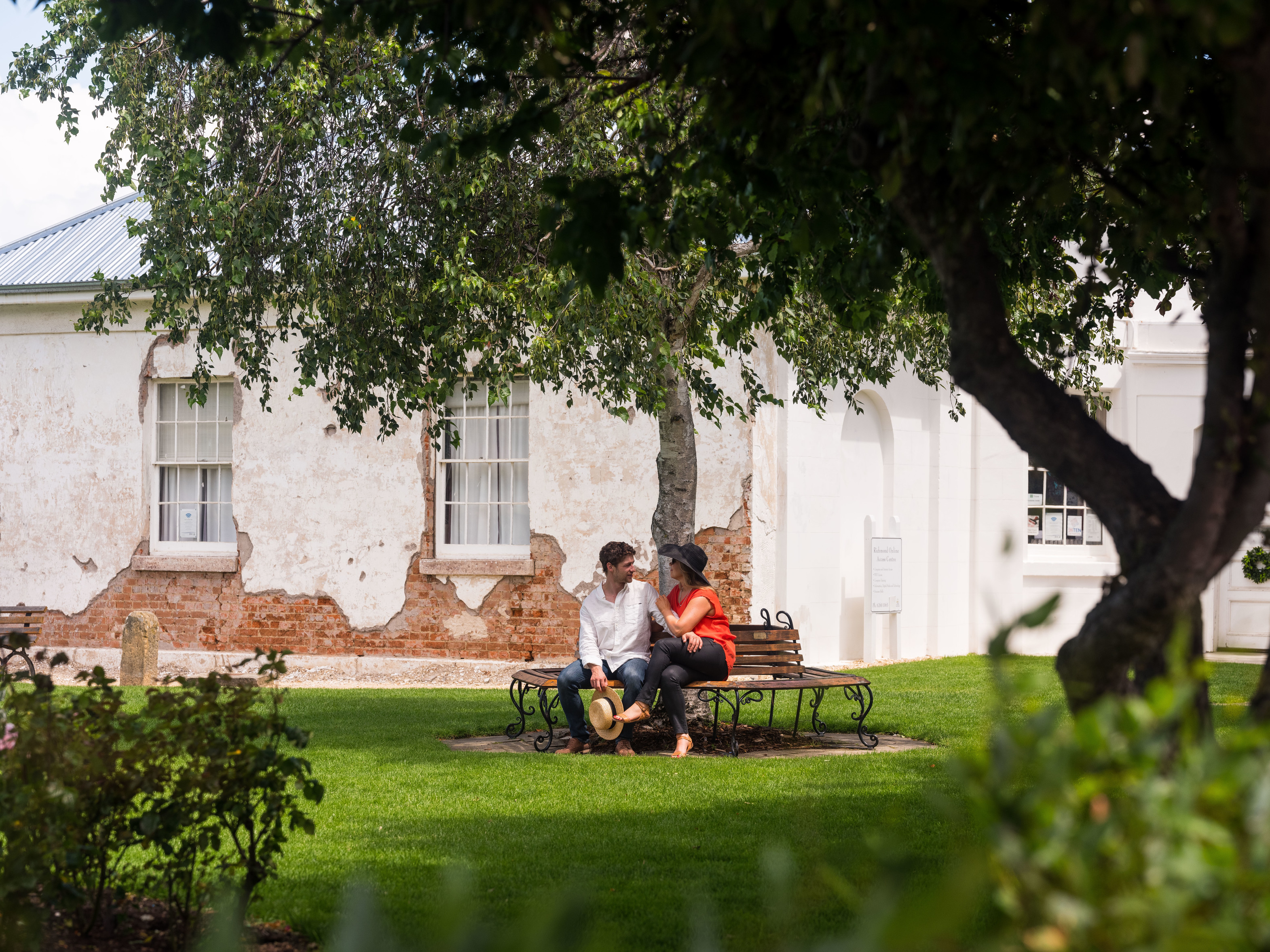 "Couple talking to each other on a bench, underneath a big tree at  Village Green, Richmond"
