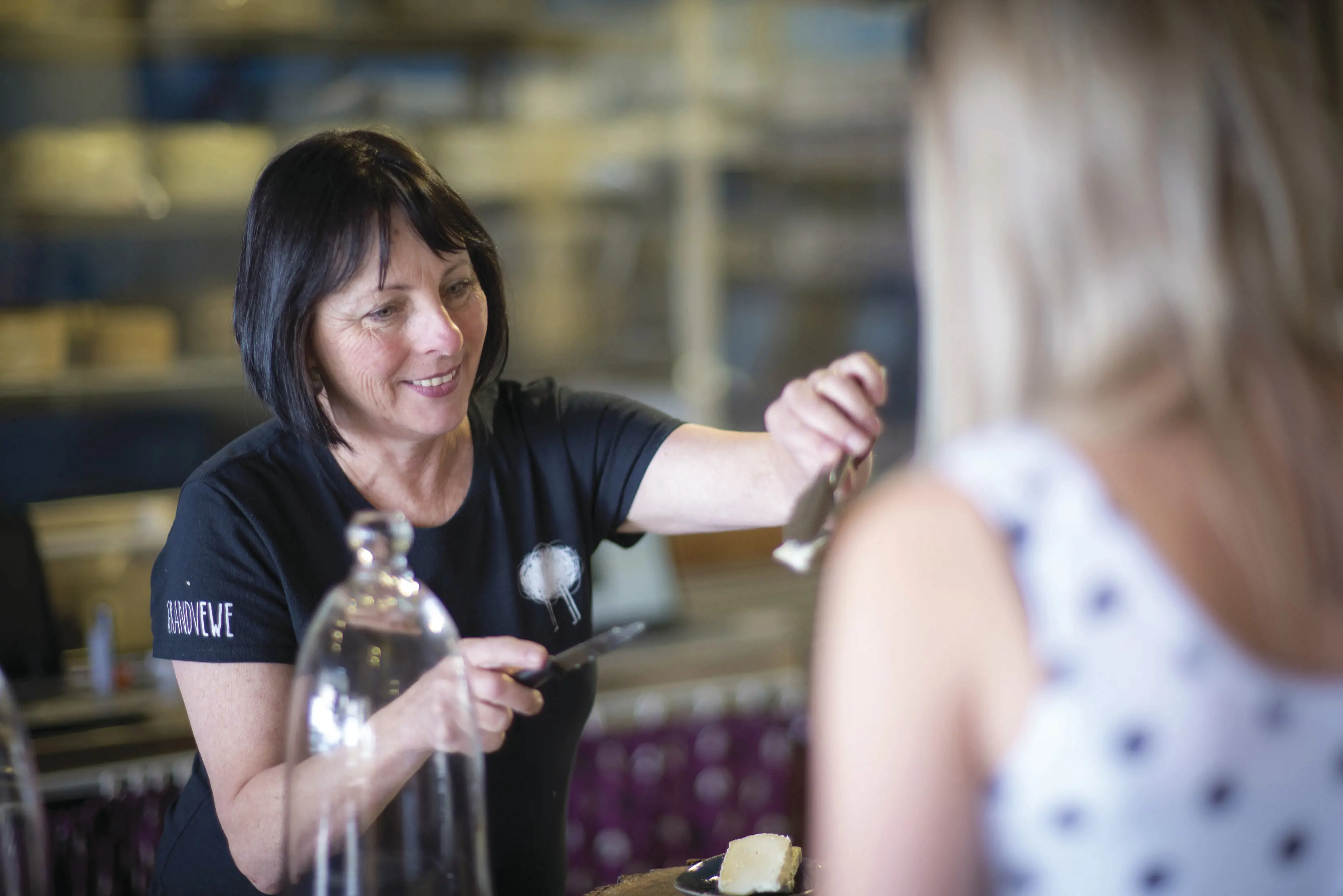 A woman hands someone a slice of cheese at a cheese tasting class at Grandvewe Cheeses, Birches Bay.