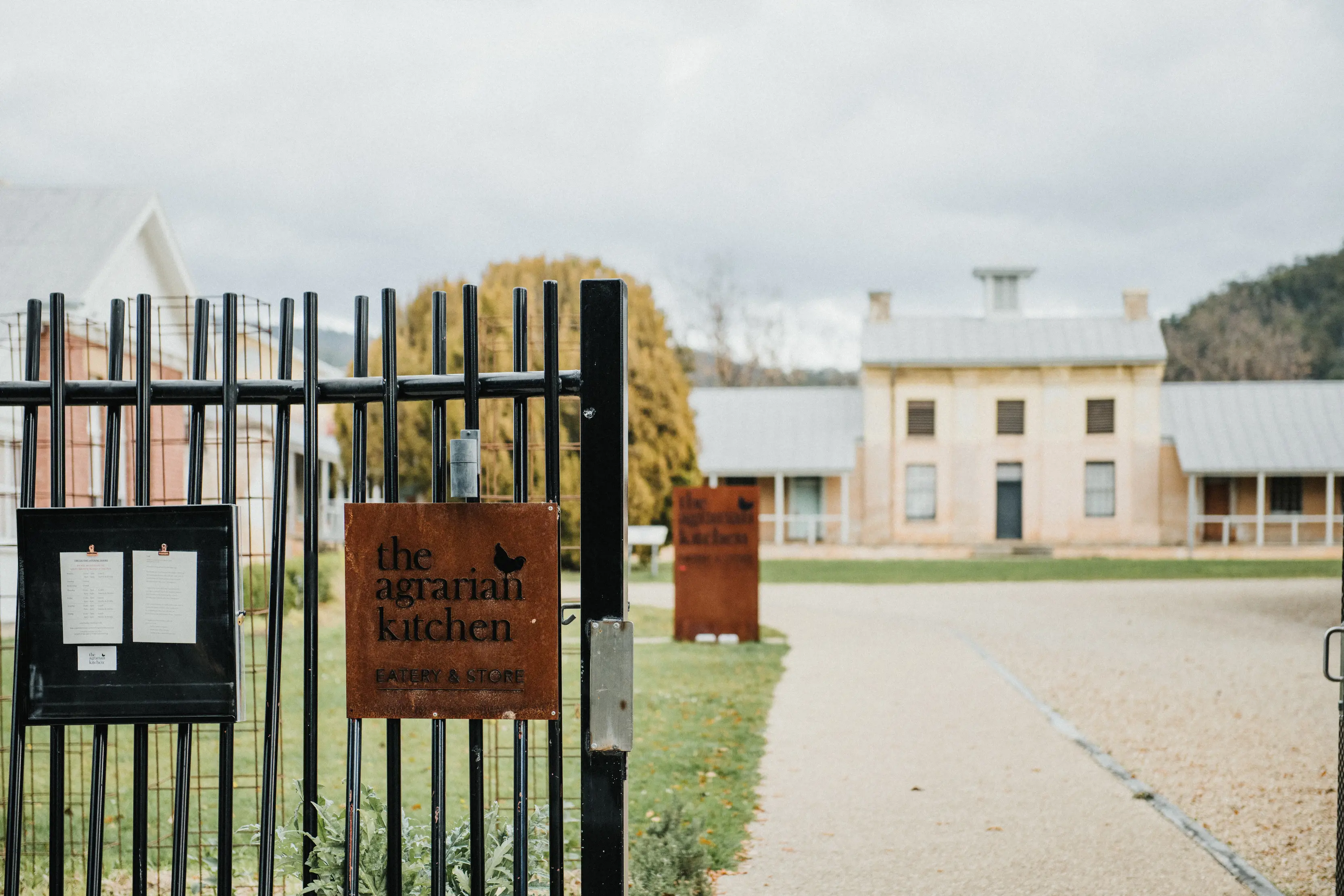 A fence with a sign reading 'The Agrarian Kitchen' with a courtyard and colonial buildings in the background.