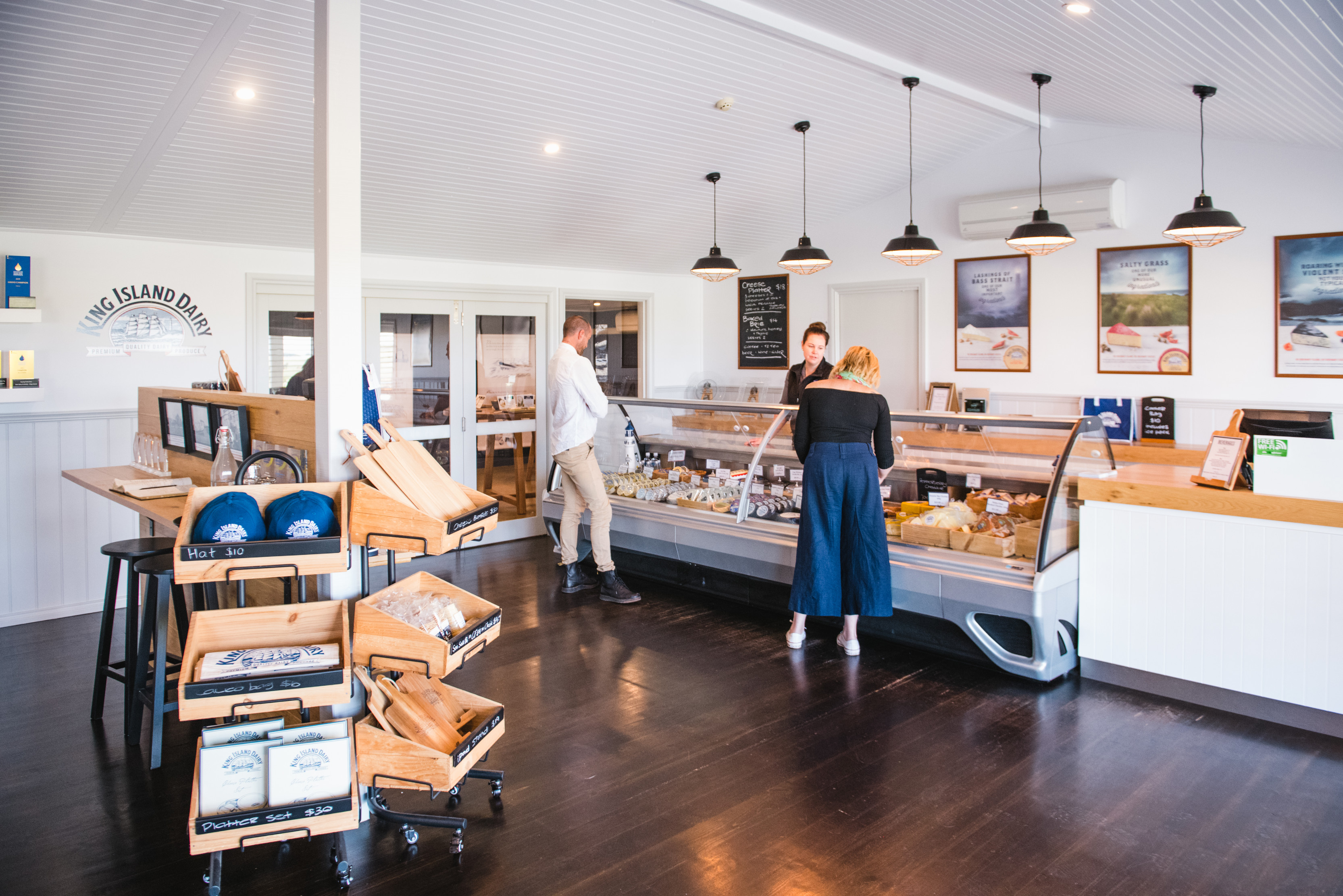 Image of inside the King Island Dairy. Two customers are looking at a large variety of cheeses in the display.