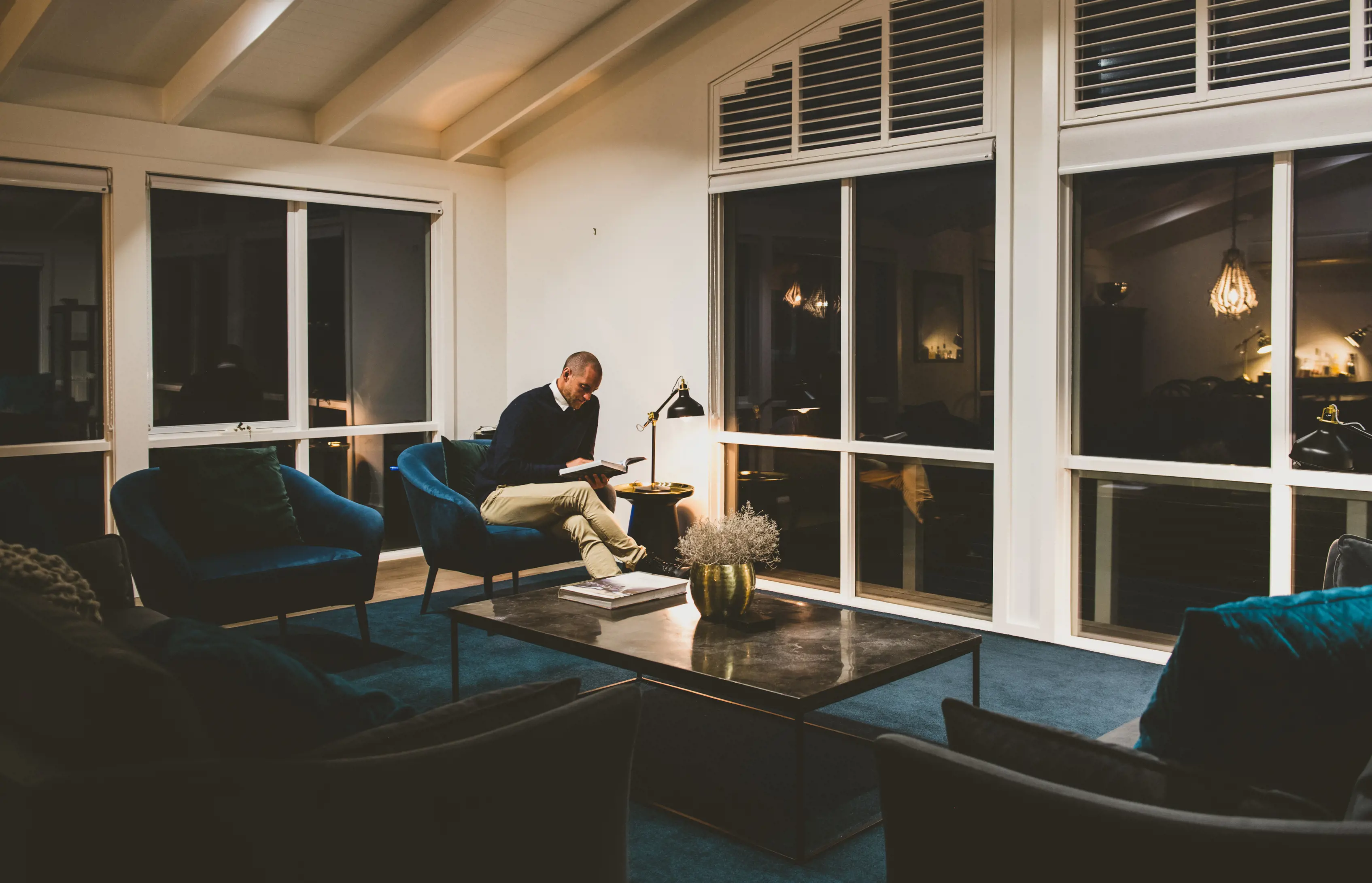 Man reading a book on a comfy chair, inside the Taraki Lodge.