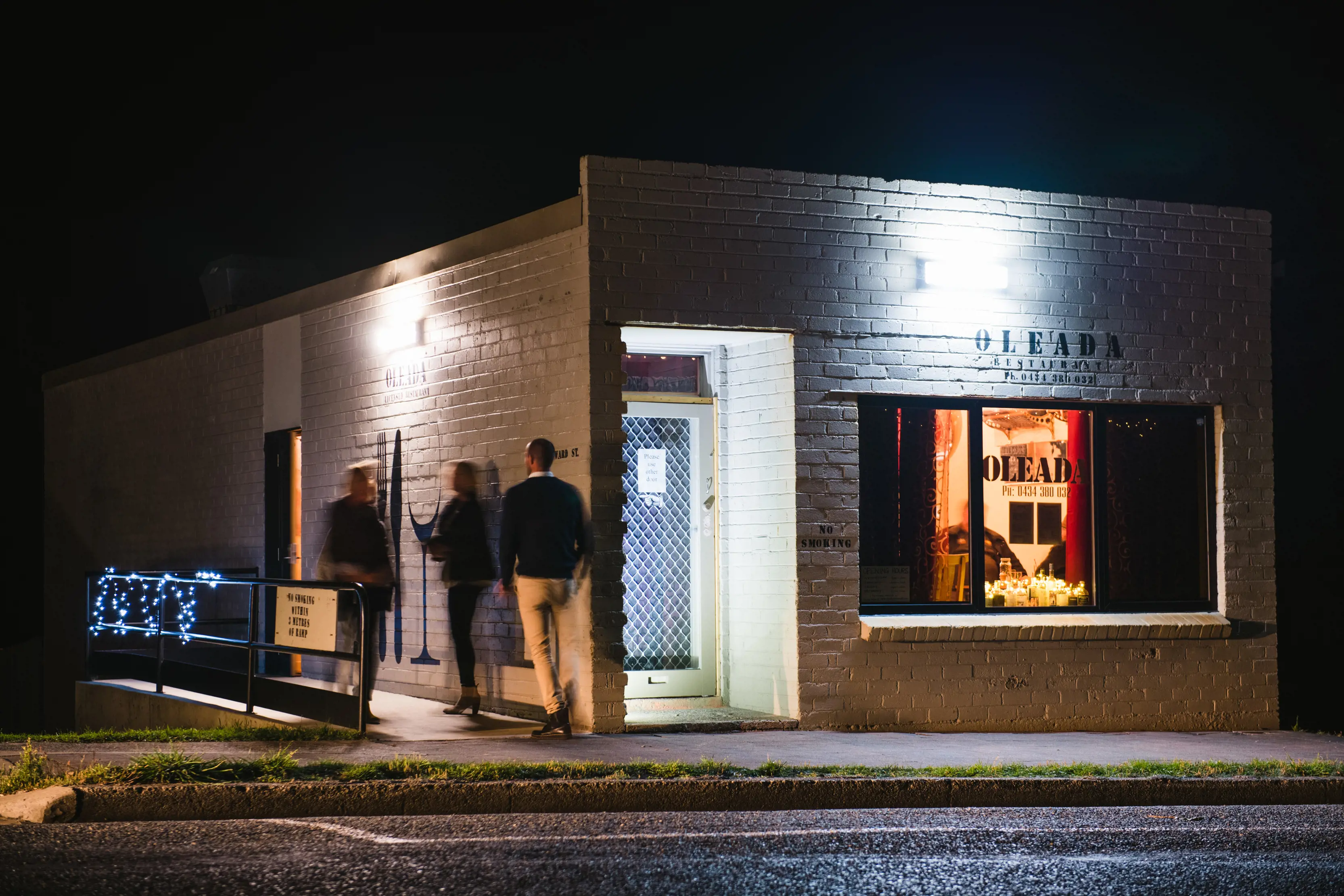 Image taken from across the road, of the Oleada restaurant, with three people walking to the entrance.