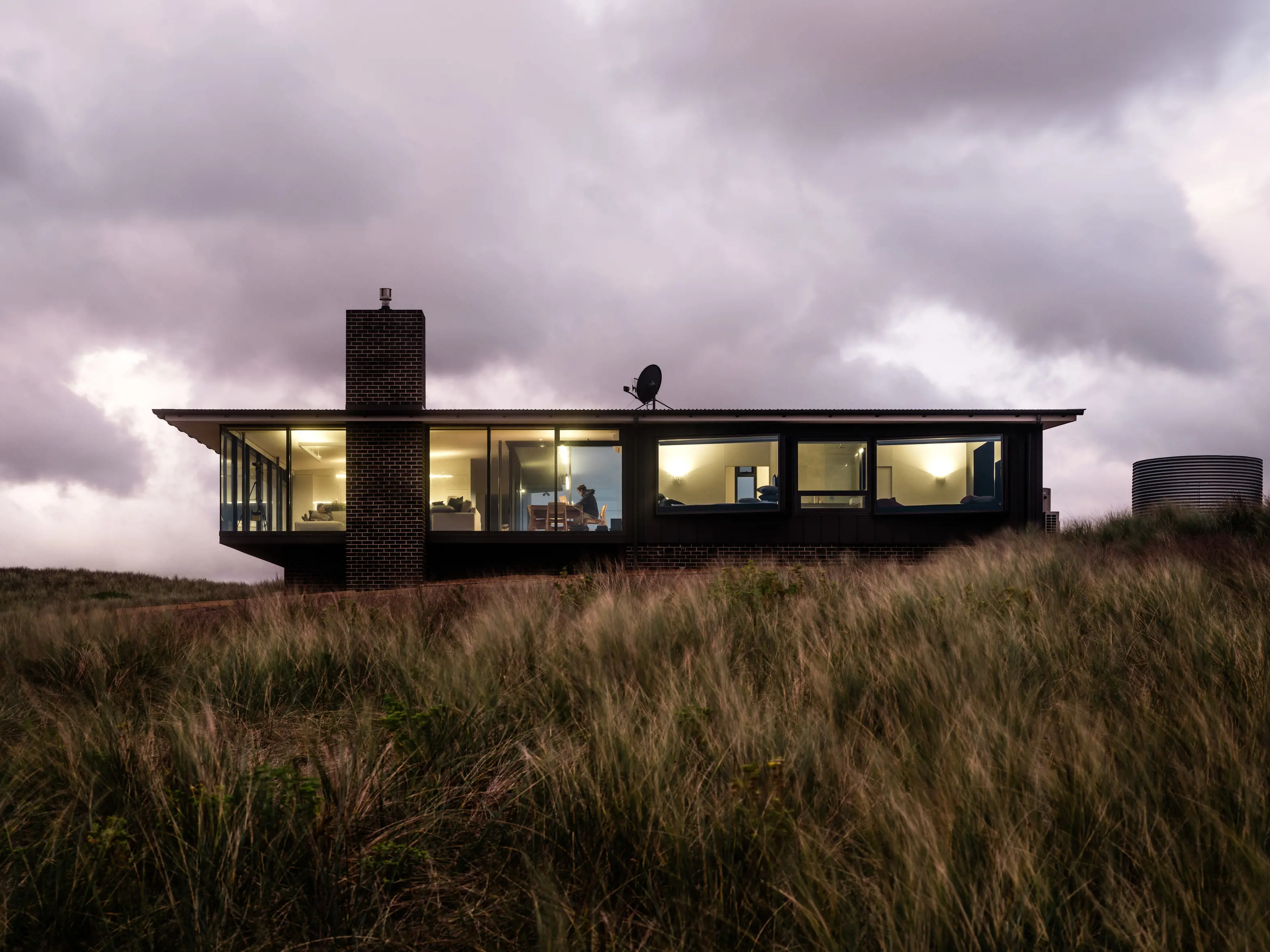 Low angle image of one of the fully glazed luxury coastal retreats with bush filling the foreground, located in Ettrick Rocks.