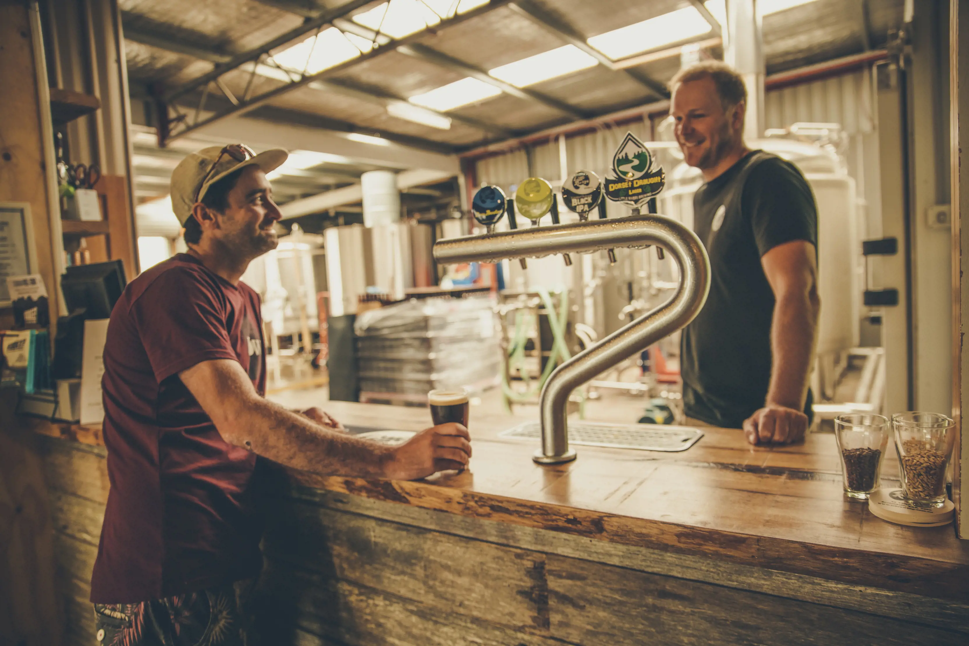 A man orders a drink over the wooden bar at Little Rivers Brewing Co., the brewery is in the background.