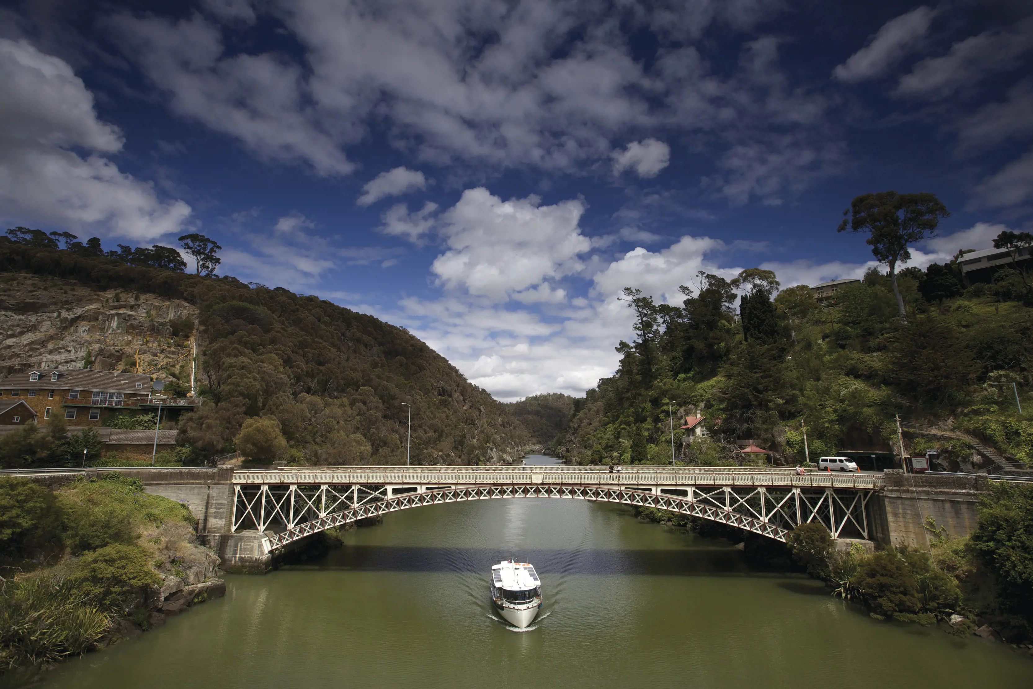 A white boat travels under Kings Bridge, at Cataract Gorge Reserve.
