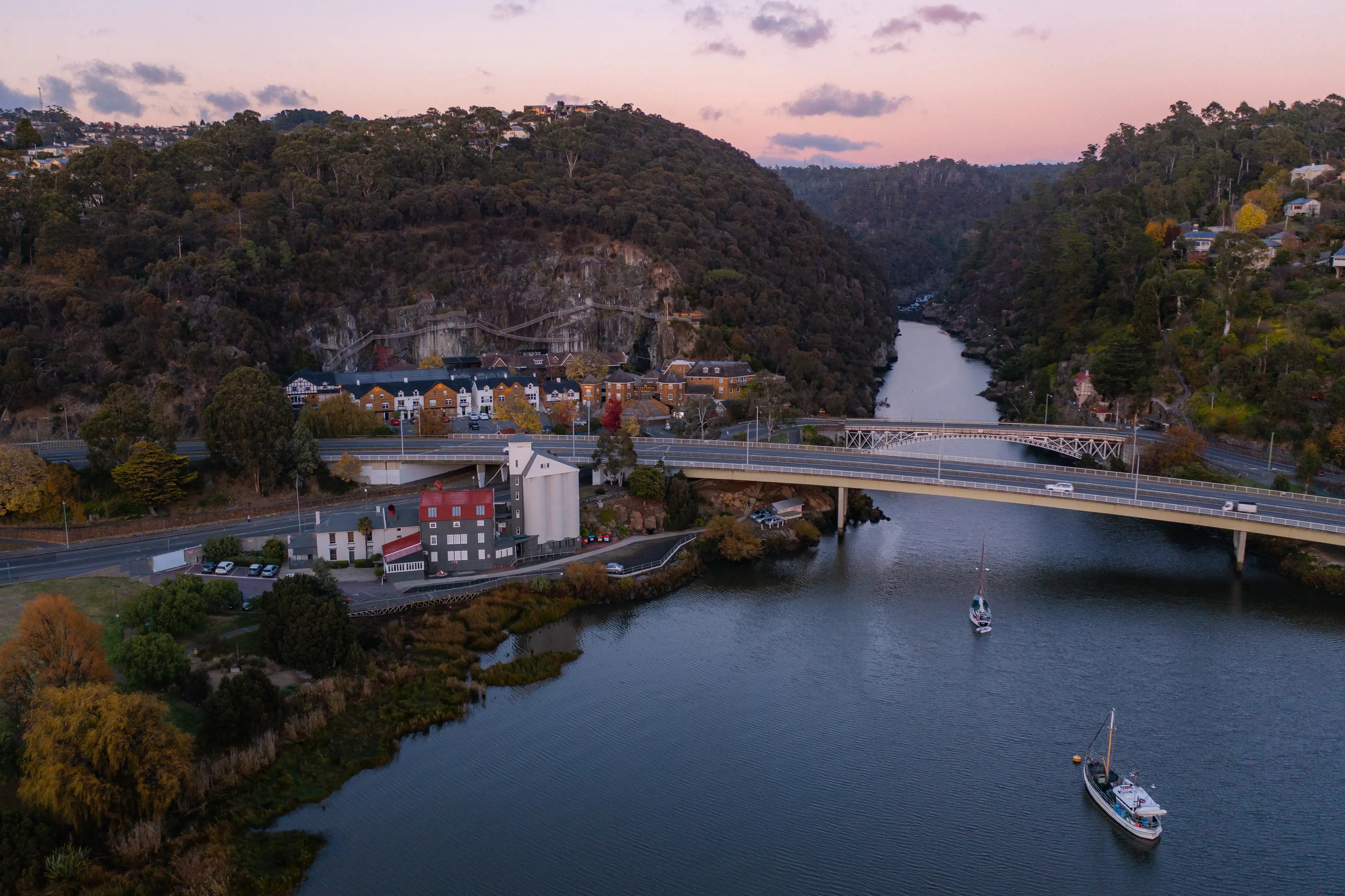 Aerial shot of Kings Bridge, Cataract Gorge Reserve, with pink skies in the backdrop and boats in the river.