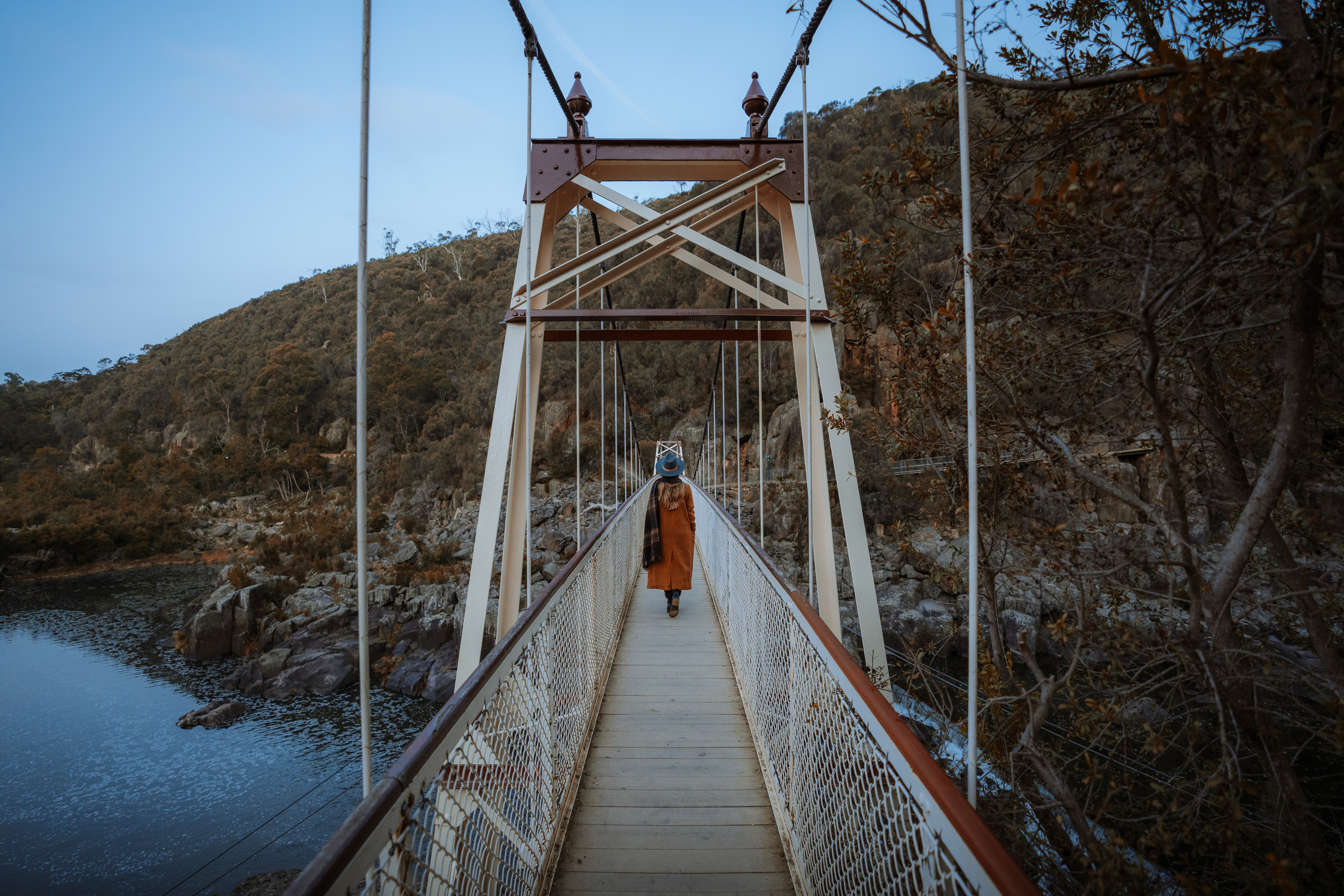 Woman walks with her back to camera across the white Alexandra Suspension bridge, Cataract Gorge Reserve.