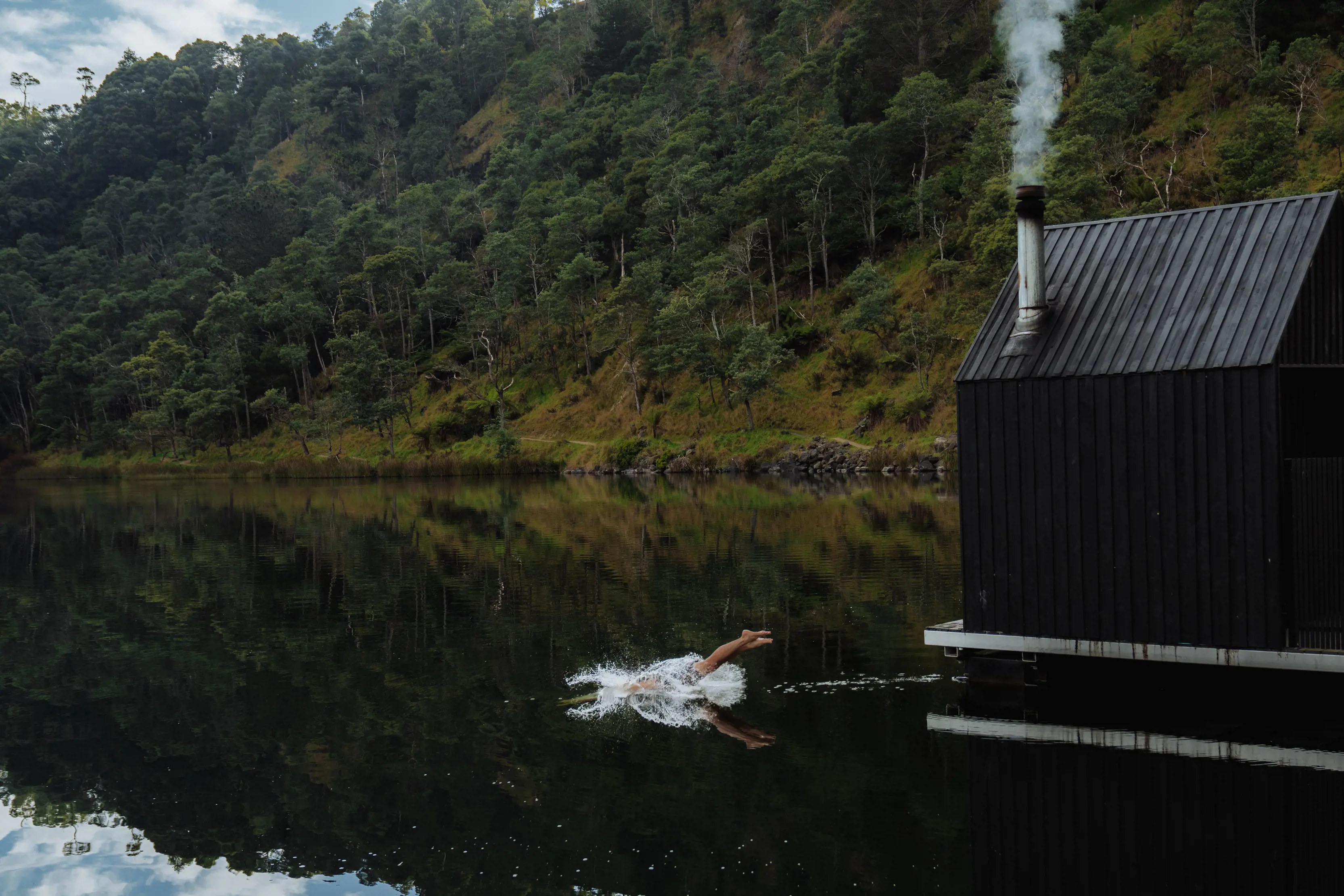 A man dives into the lake from the decking in front of the waterfront saunas at Floating Sauna Lake Derby.