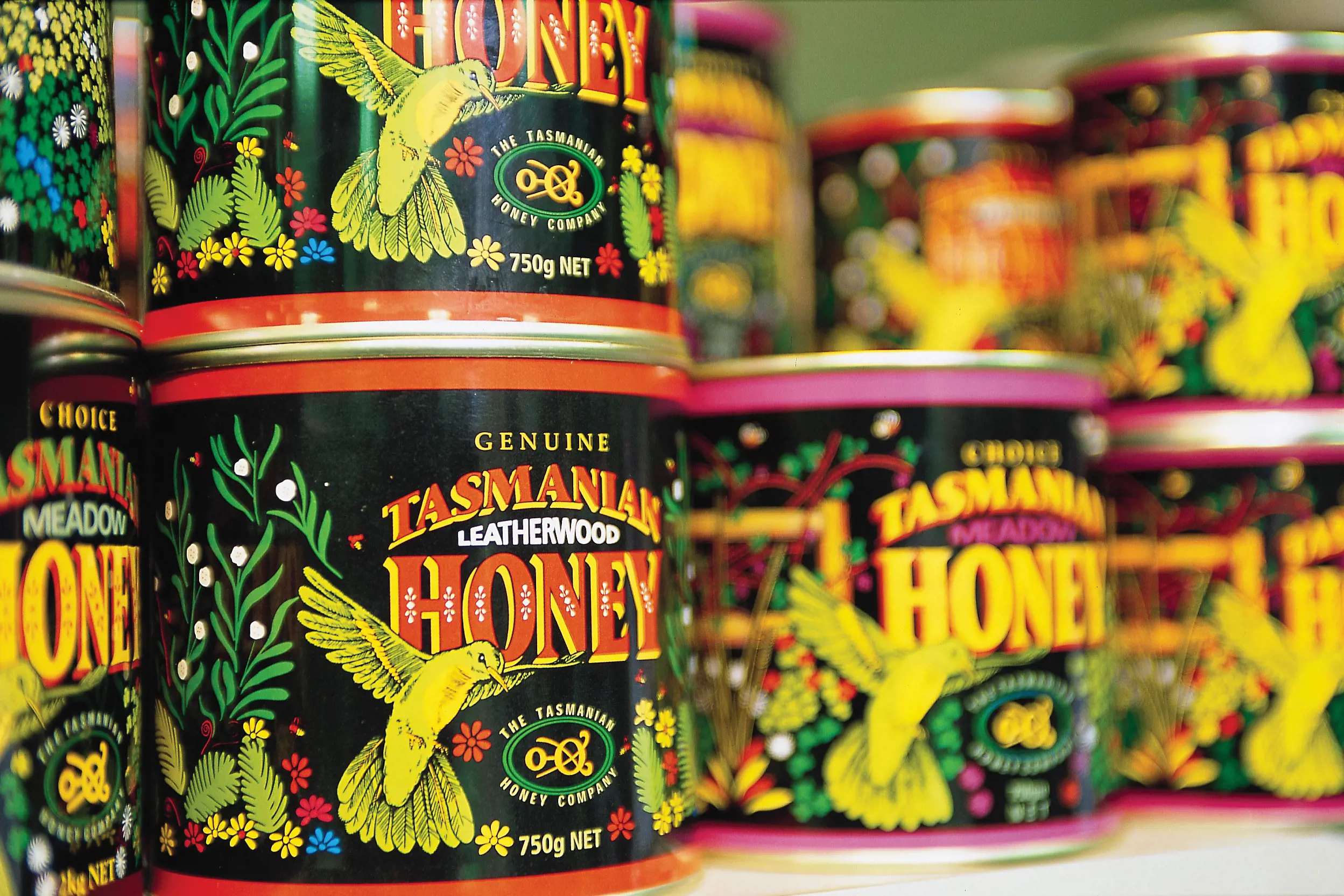 Close up of Tasmanian Honey Company products on shelf. Packaging is black with colourful bird and flower decoration.