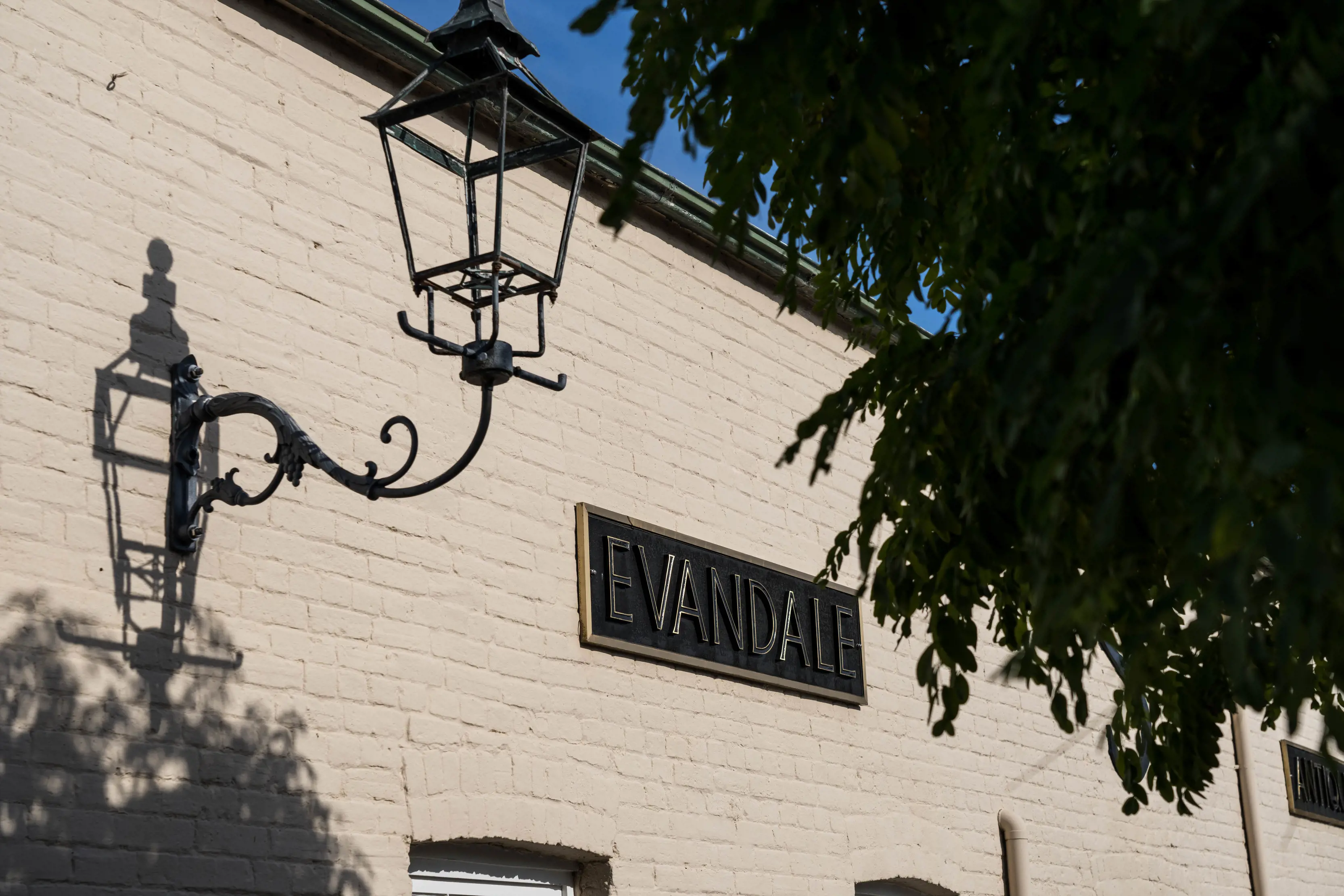 Exterior light and black Evandale sign on a white brick wall outside Evandale Antiques.