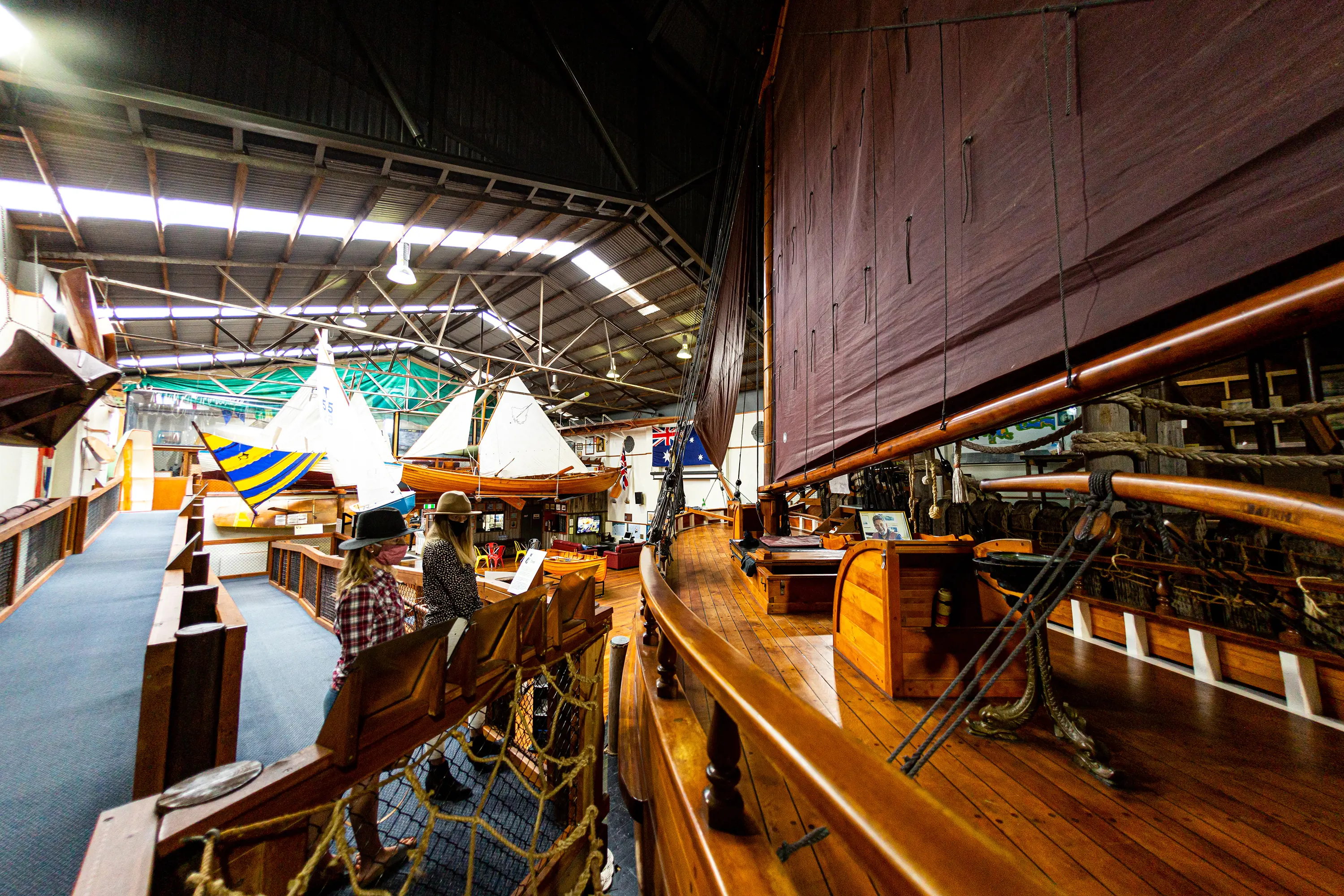 Two young women examine the polished woodwork on an old wooden boat.