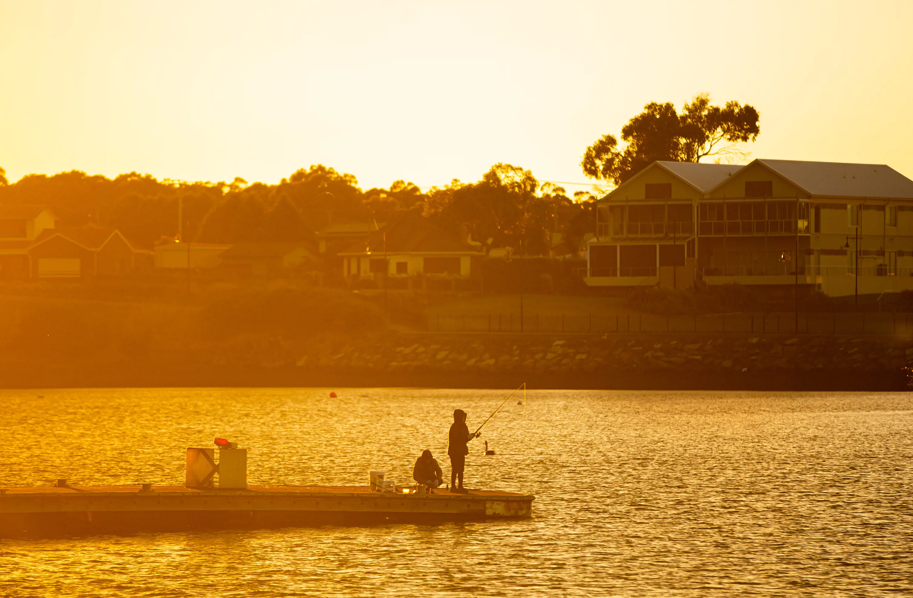 Two boys fish form the end of a long pier at the George Town waterfront at dusk.