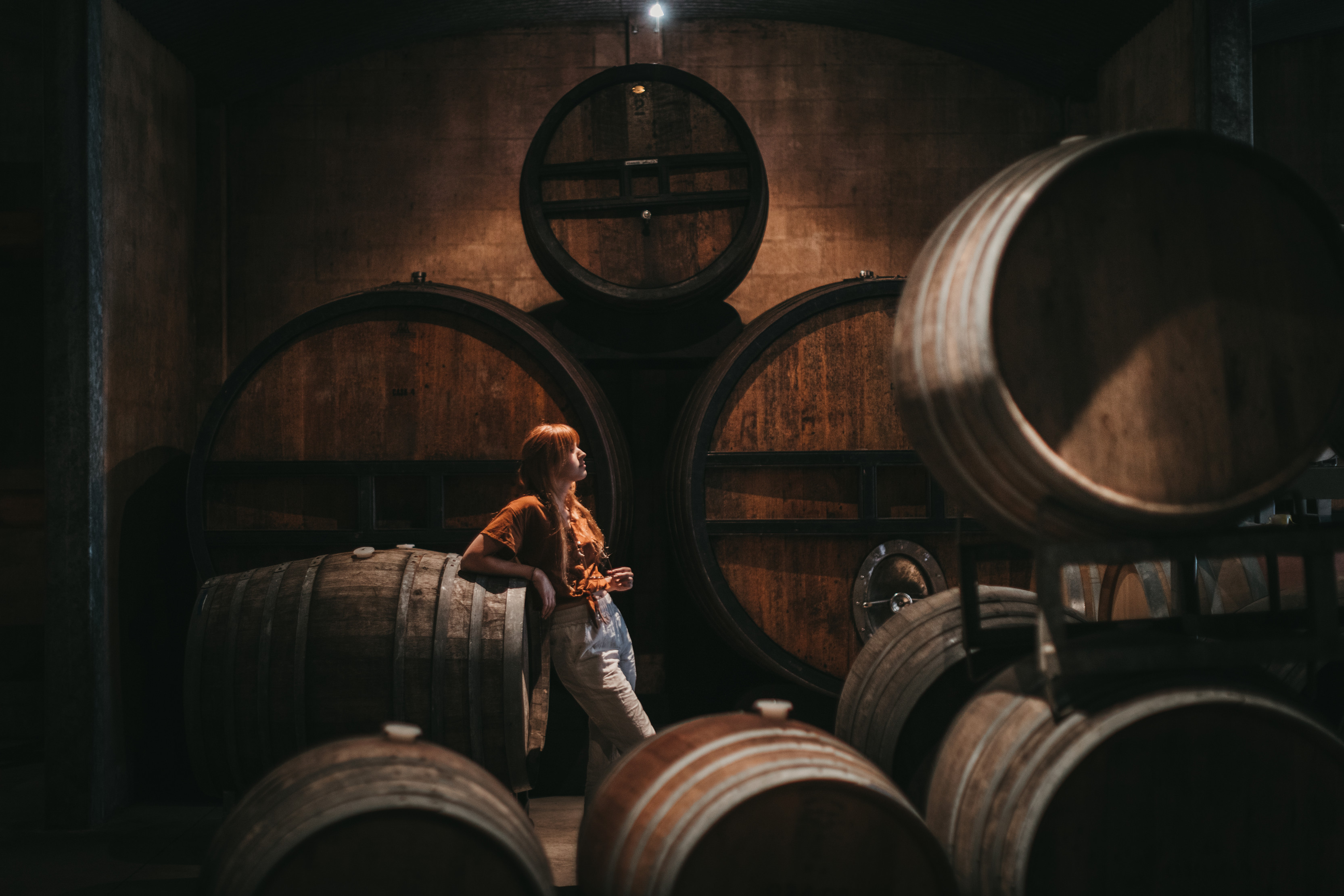 Interior of a woman with red hair surrounded by barrells at Pipers Brook Vineyard.