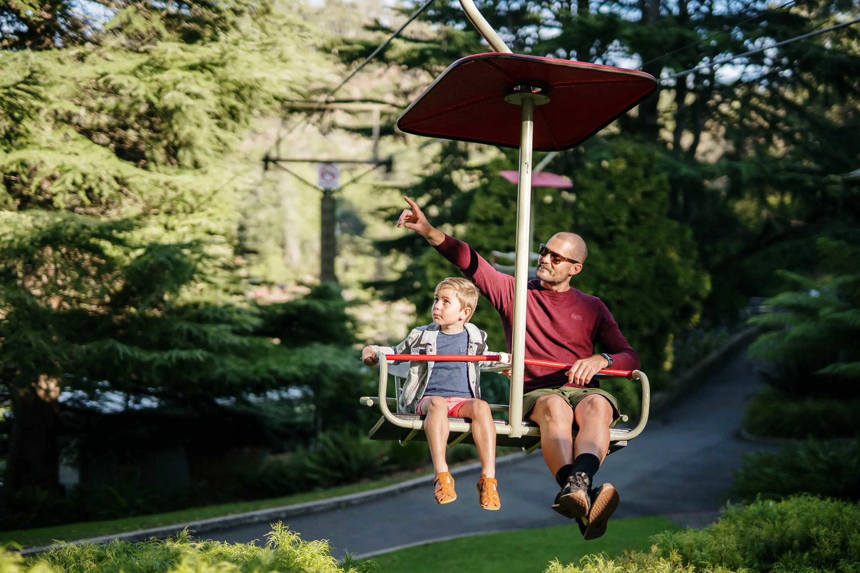 A father and his young son ride the chair lift above a garden.