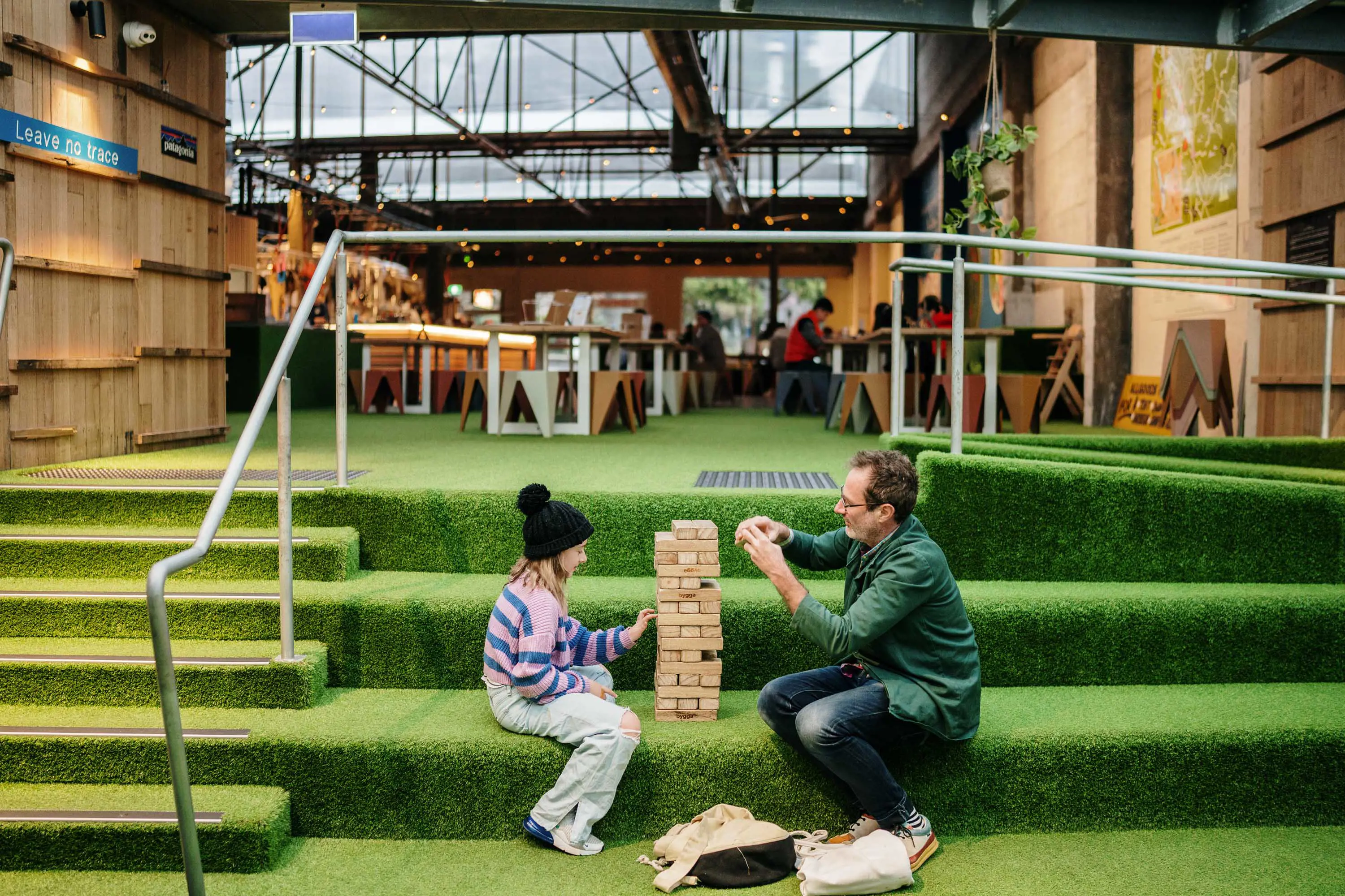 A father and daughter sit on steps inside a large. converted warehouse brewery and play a game.