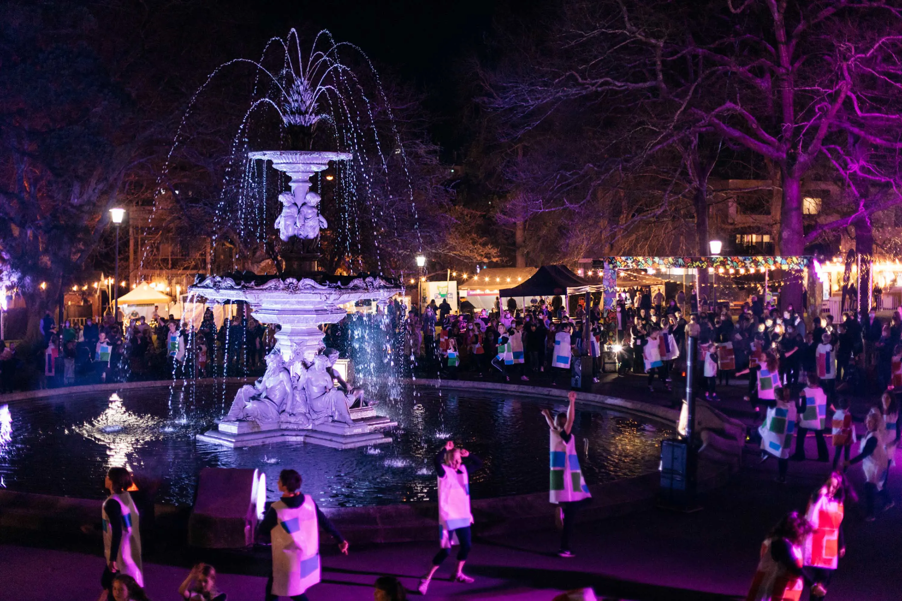 People enjoy a night festival with stalls and lights with a large fountain at its centre.