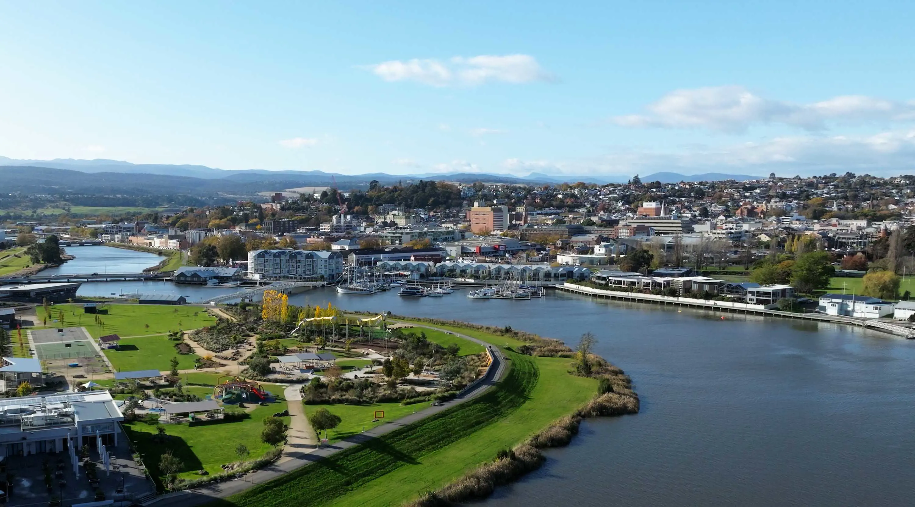 An aerial view of Launceston looking across the Tamar River, with a large park in the foreground and the city in the background.
