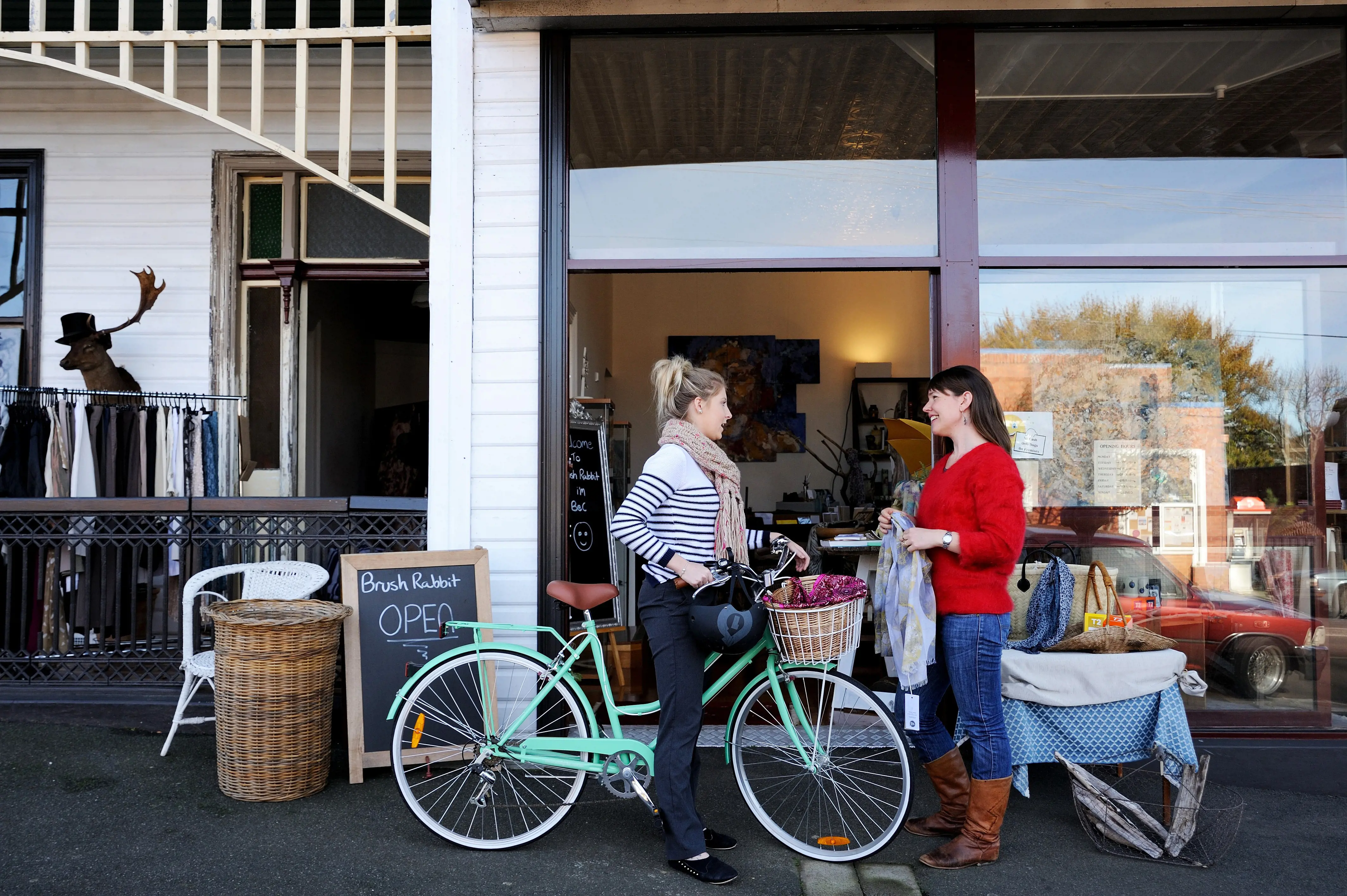 A woman in a striped top stops her bicycle to chat to a woman in a red top outside a Deloraine shop.