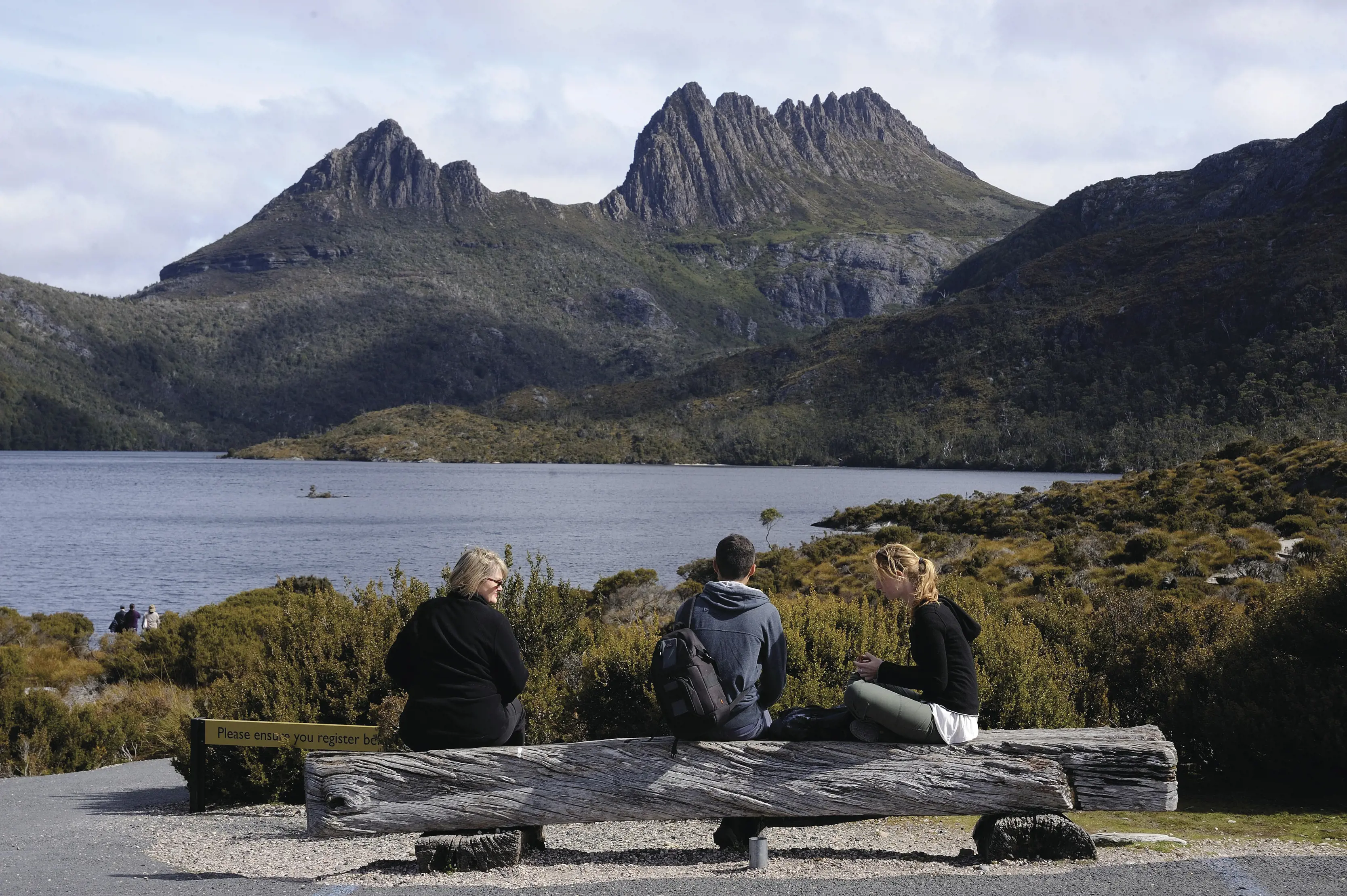 "Three people sitting by Dove Lake, looking at the stunning landscape that leads to Cradle Mountain in the background. "
