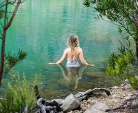 Incredible image of a woman walking into a tranquil, vibrant blue pool, surrounded by lush bushland.