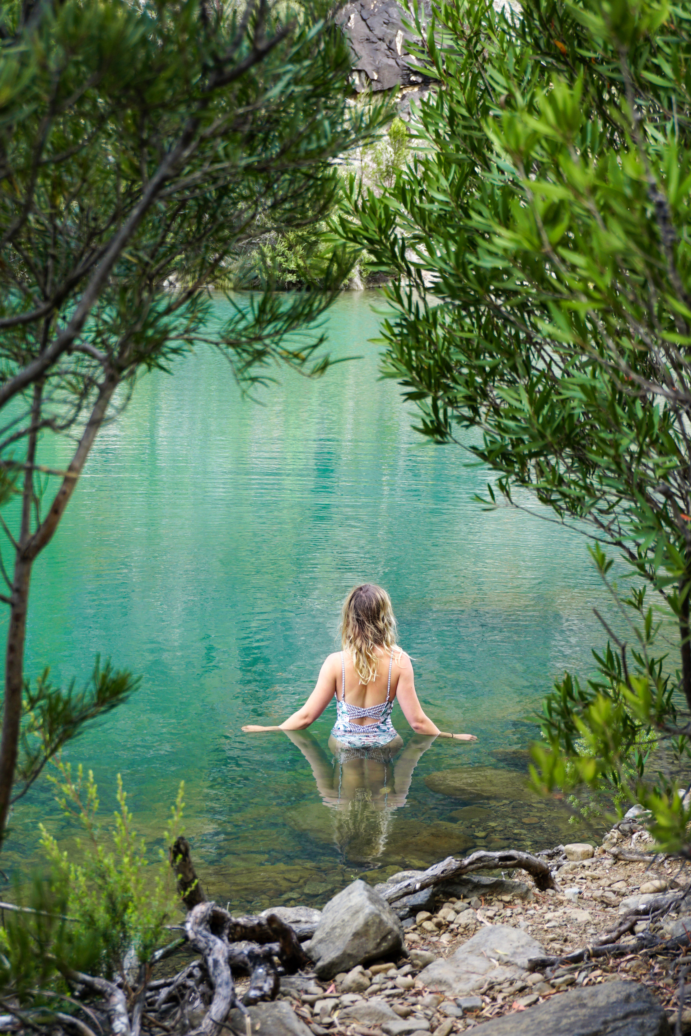 Incredible image of a woman walking into a tranquil, vibrant blue pool, surrounded by lush bushland.